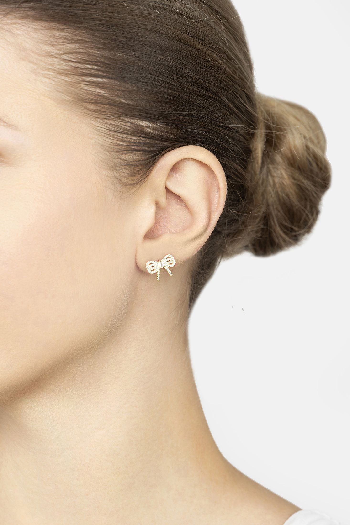 Close-up of a person wearing gold bow-shaped earrings on a plain background