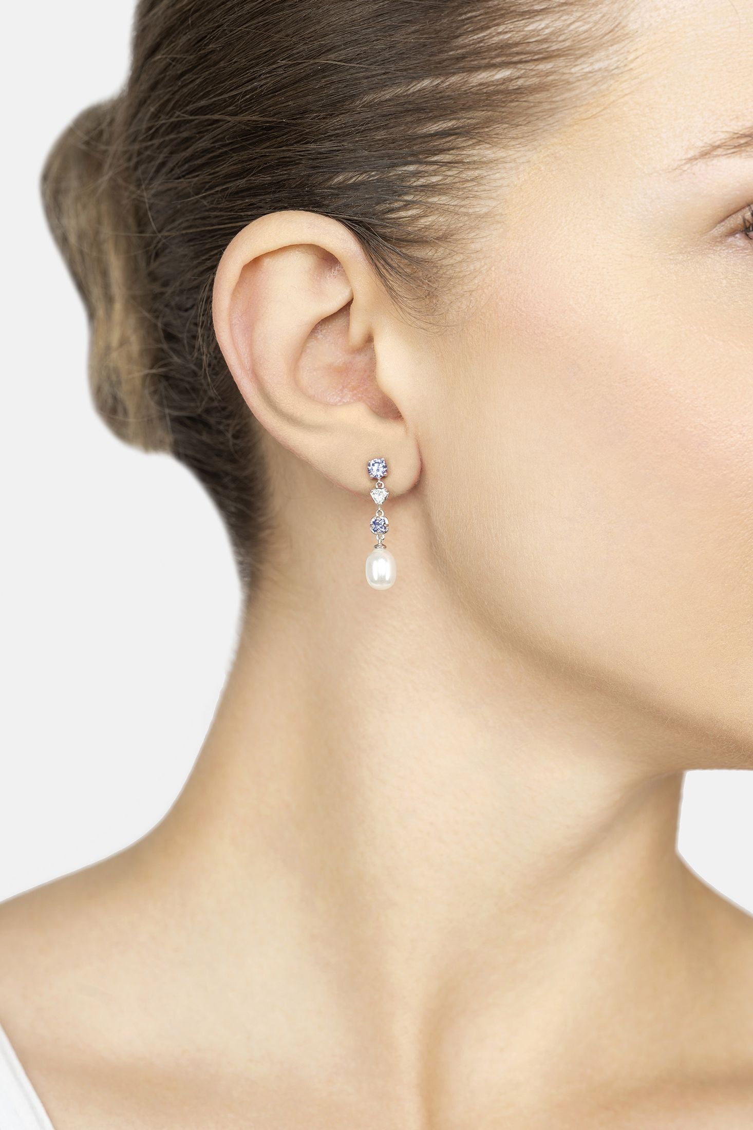 Close-up of a woman wearing a set of pearl drop earrings with a white background