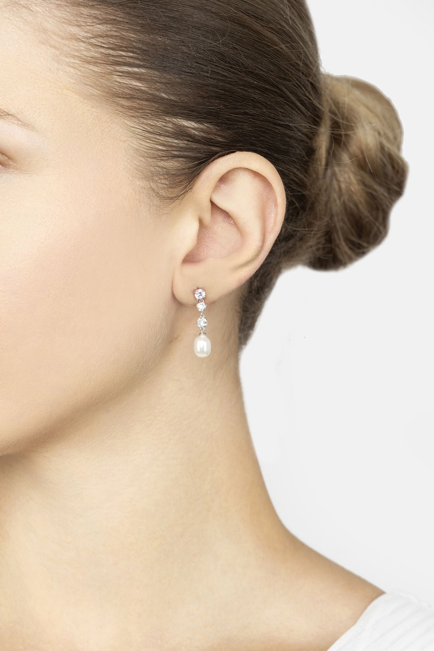 Close-up of a person wearing pearl earrings with a plain background