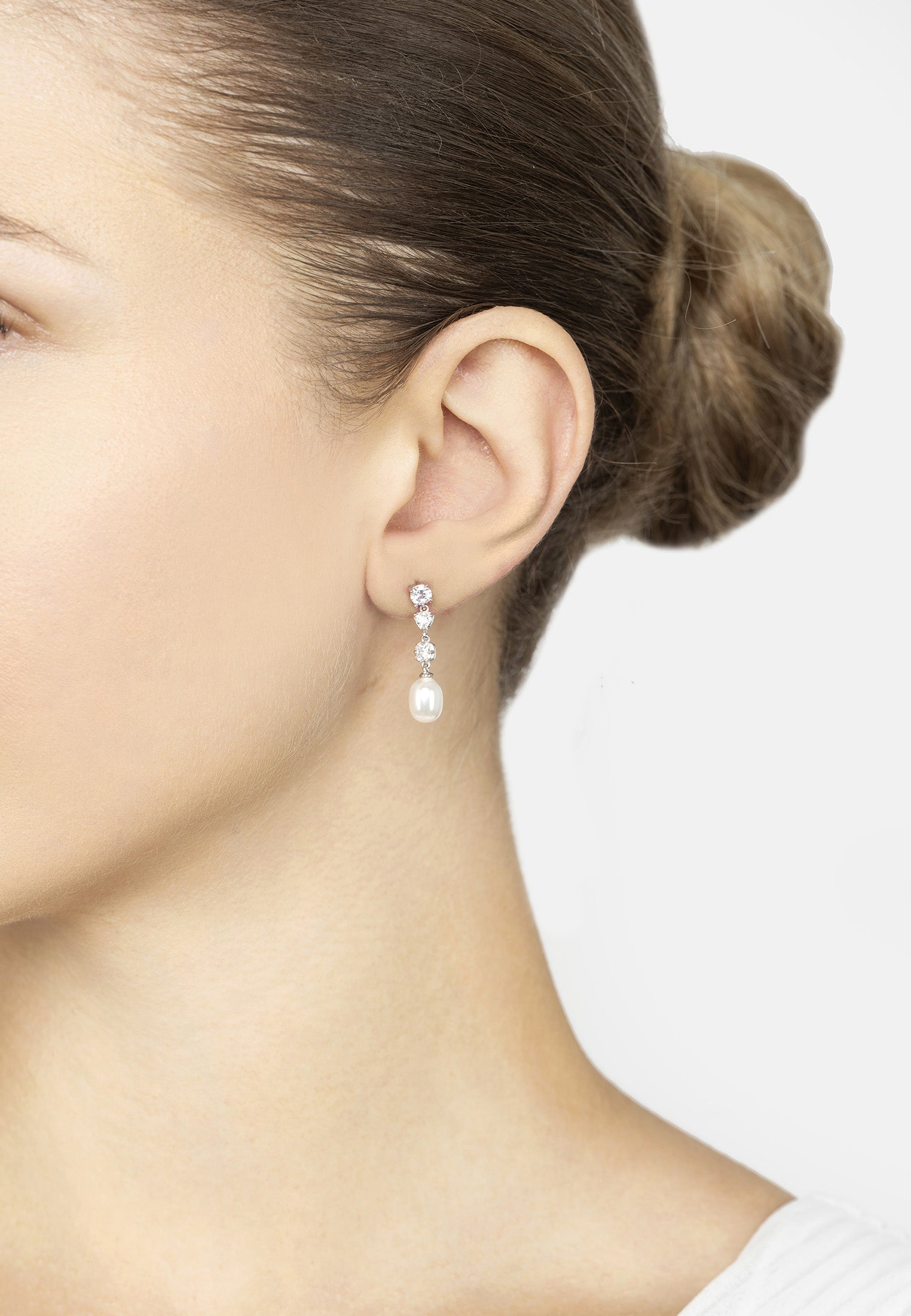 Close-up of a person wearing pearl earrings with a plain background