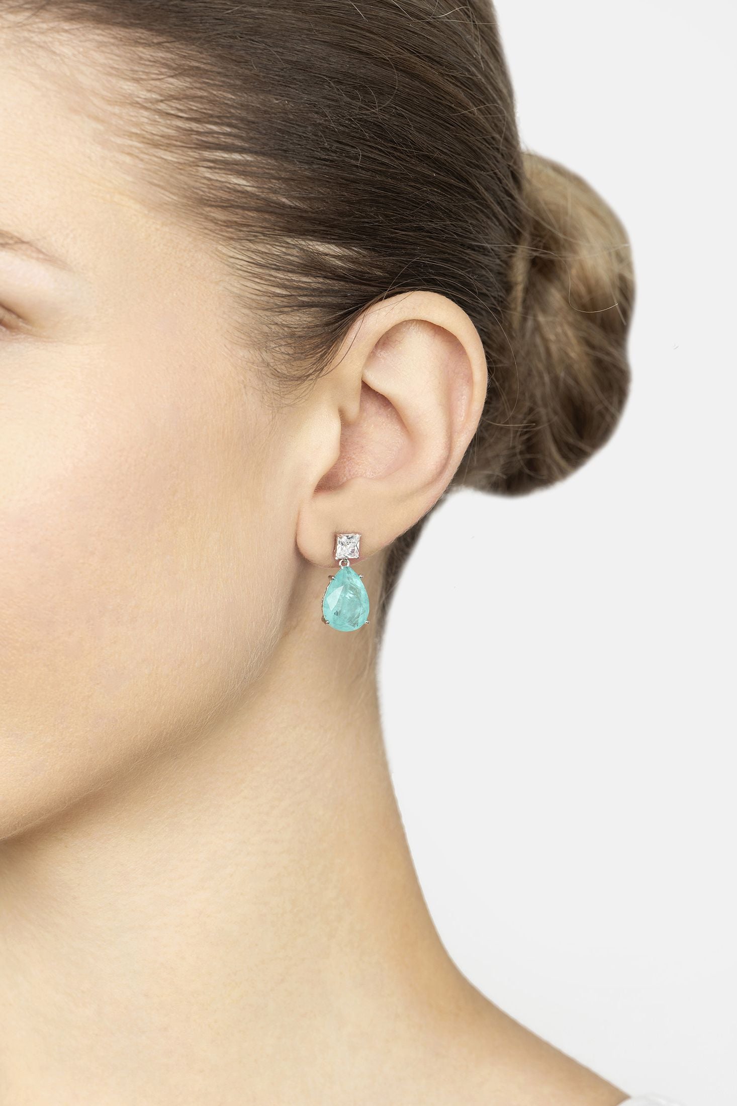 Close-up of a person wearing turquoise earrings with a neutral background