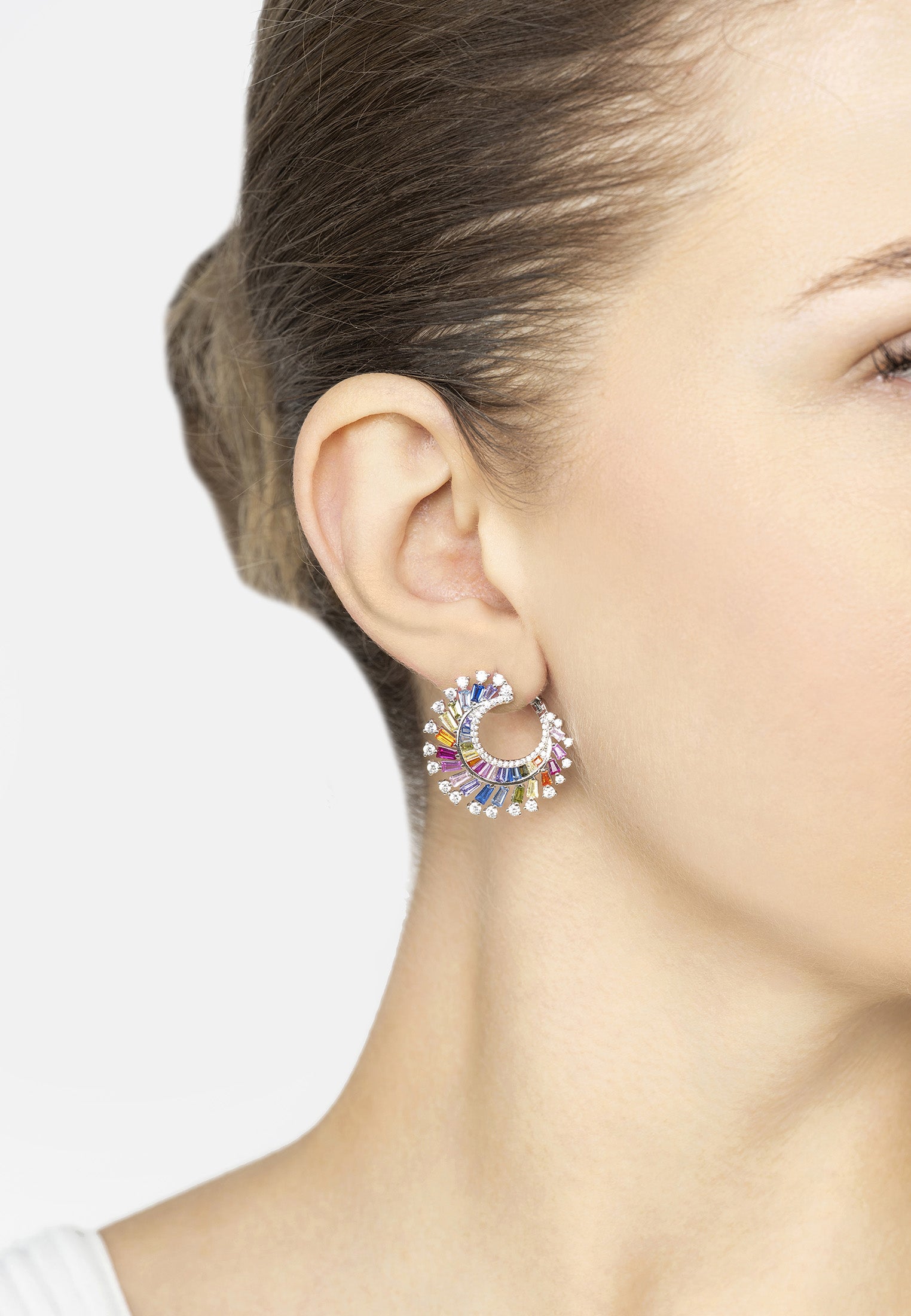 Close-up of a woman wearing colorful hoop earrings with a plain background