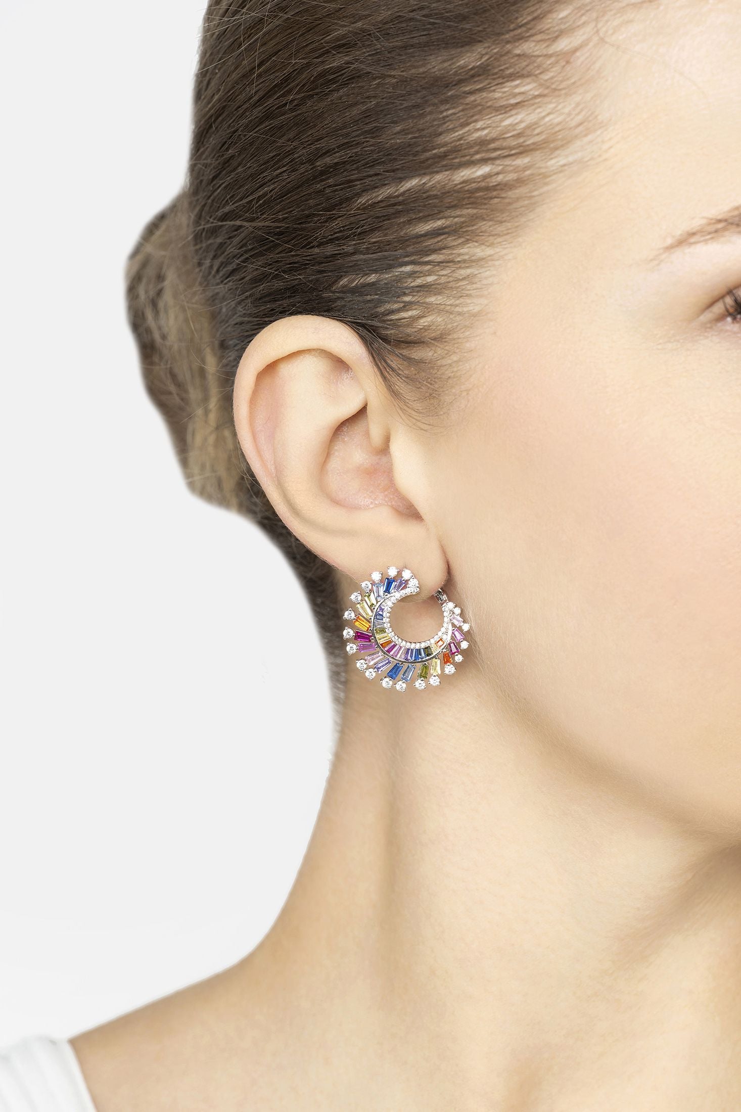 Close-up of a woman wearing colorful hoop earrings with a plain background