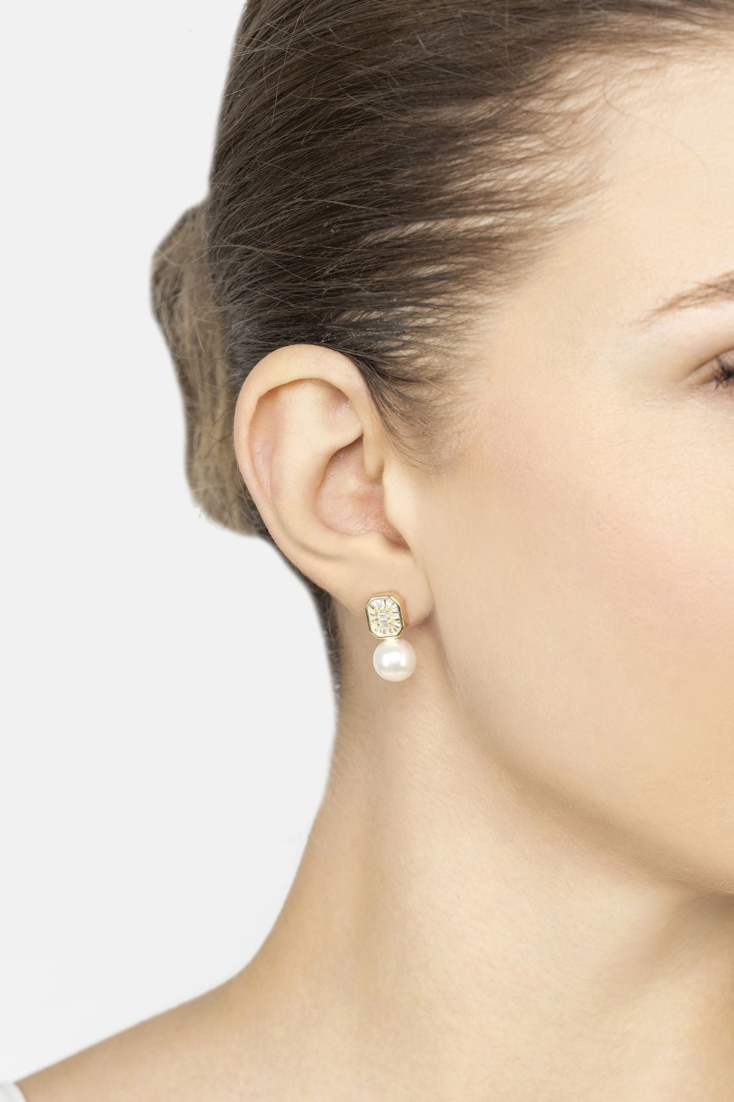 Close-up of a woman wearing pearl earrings with a plain background