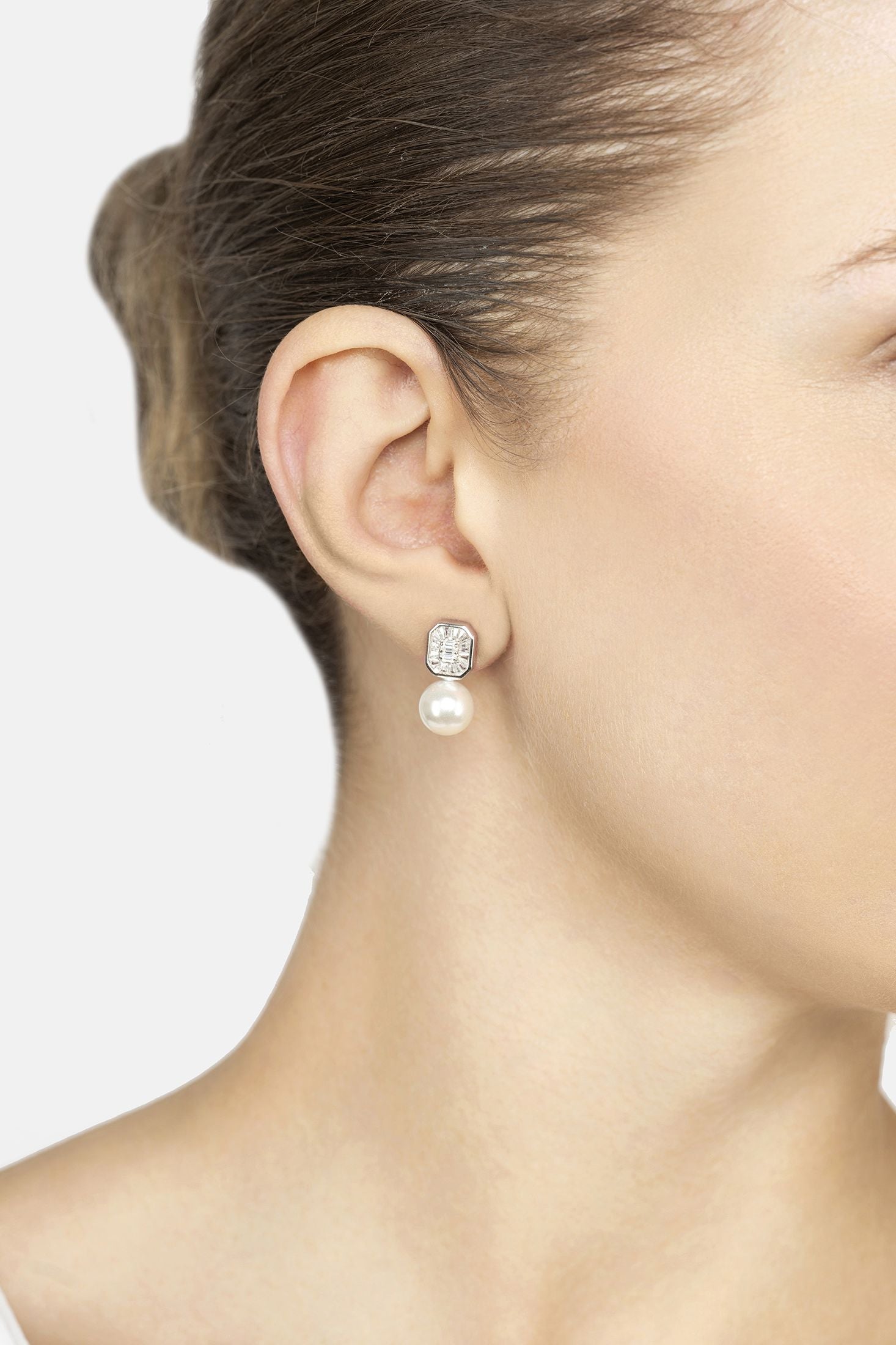 Pearl earring worn by a model on a plain background