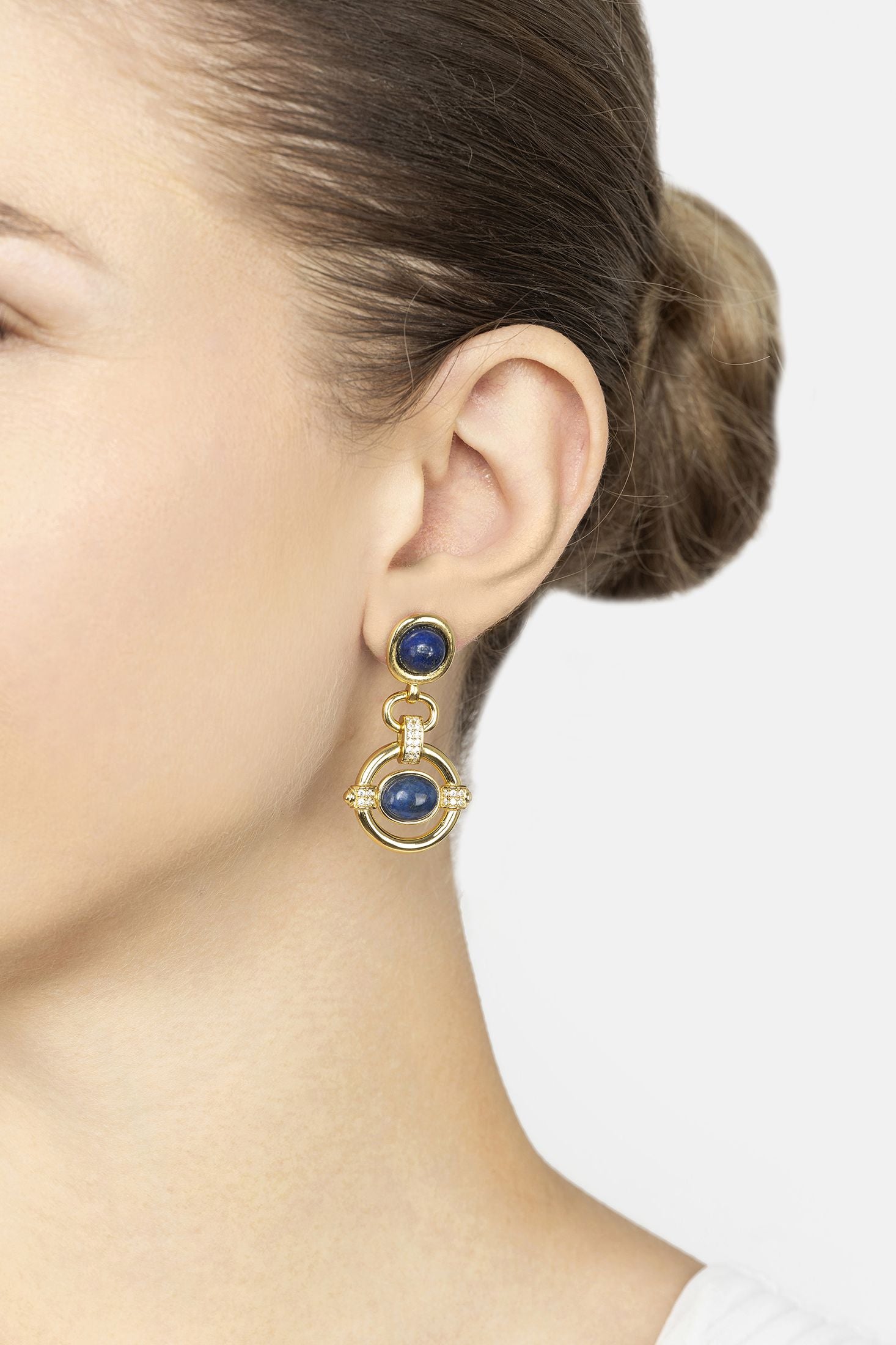 Close-up of a person wearing gold earrings with blue stones on a white background