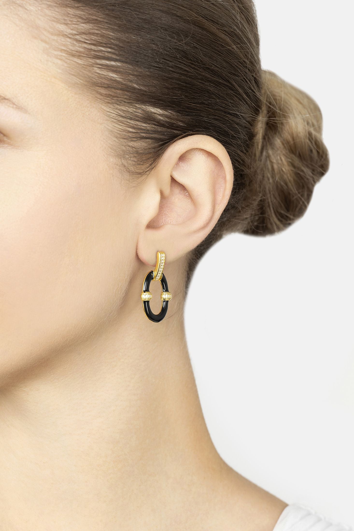 Close-up of a person wearing gold drop earrings with a black center on a white background