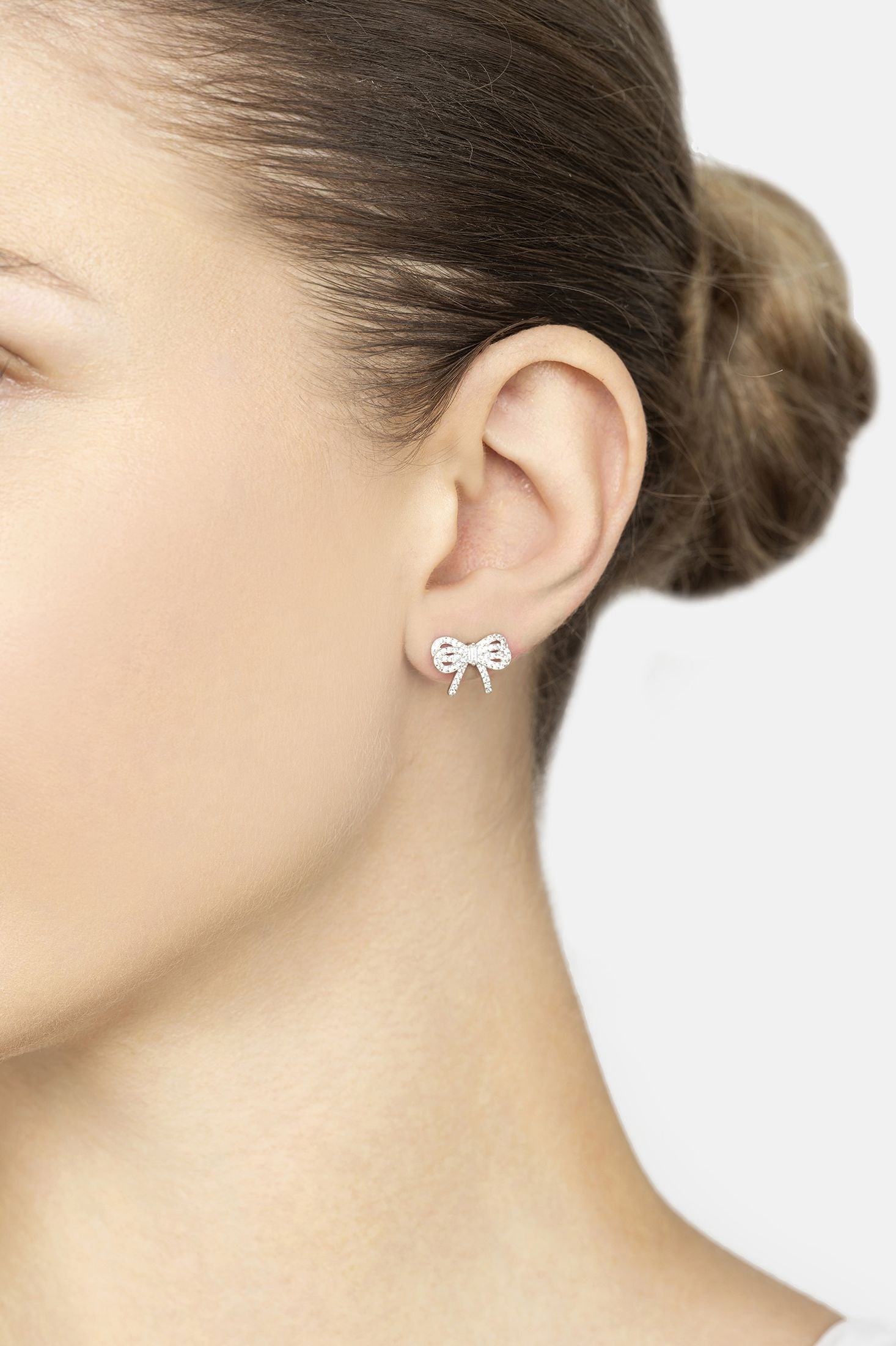 Close-up of a person wearing bow-shaped earrings with a plain background