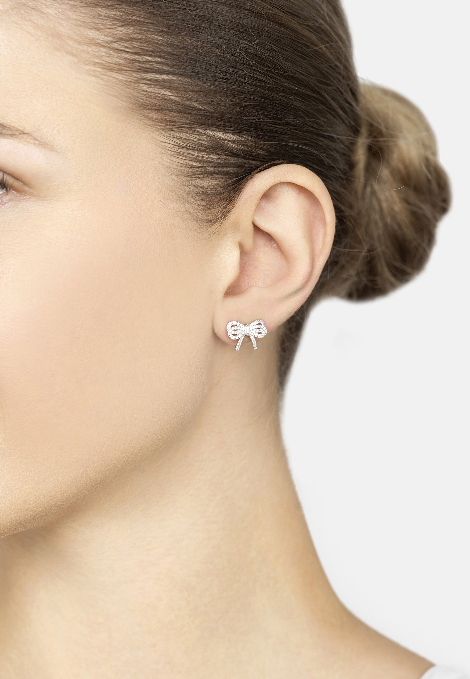 Close-up of a person wearing bow-shaped earrings with a plain background