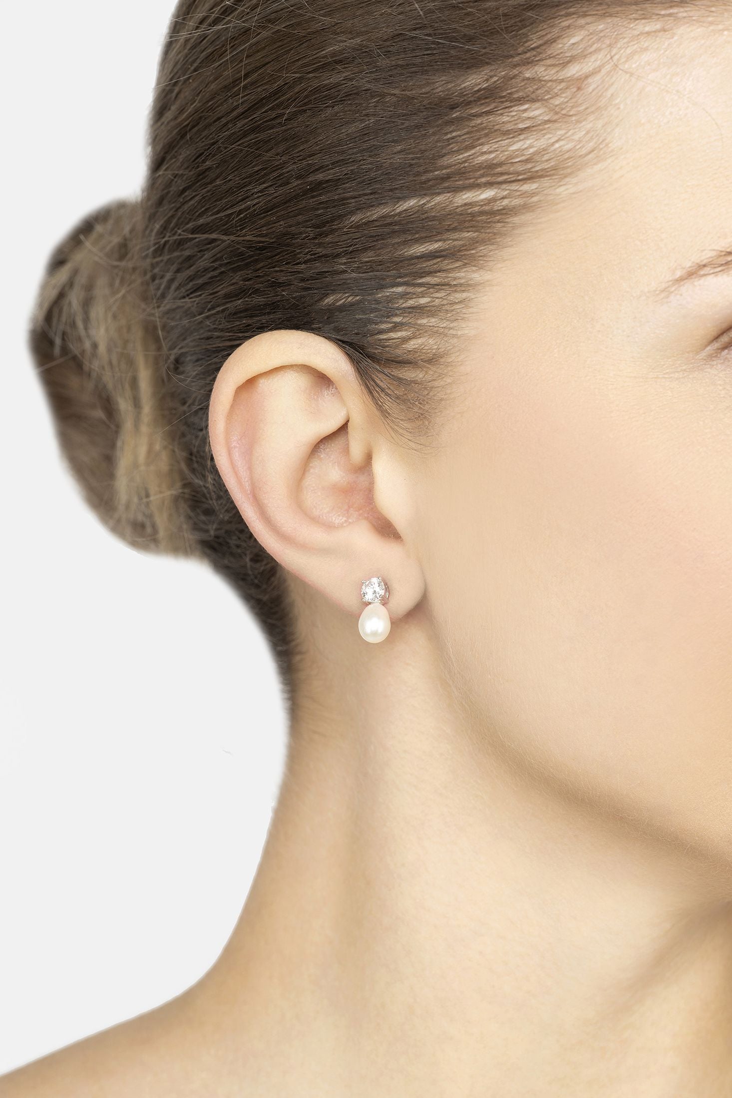 Close-up of a woman wearing pearl earrings with a plain background