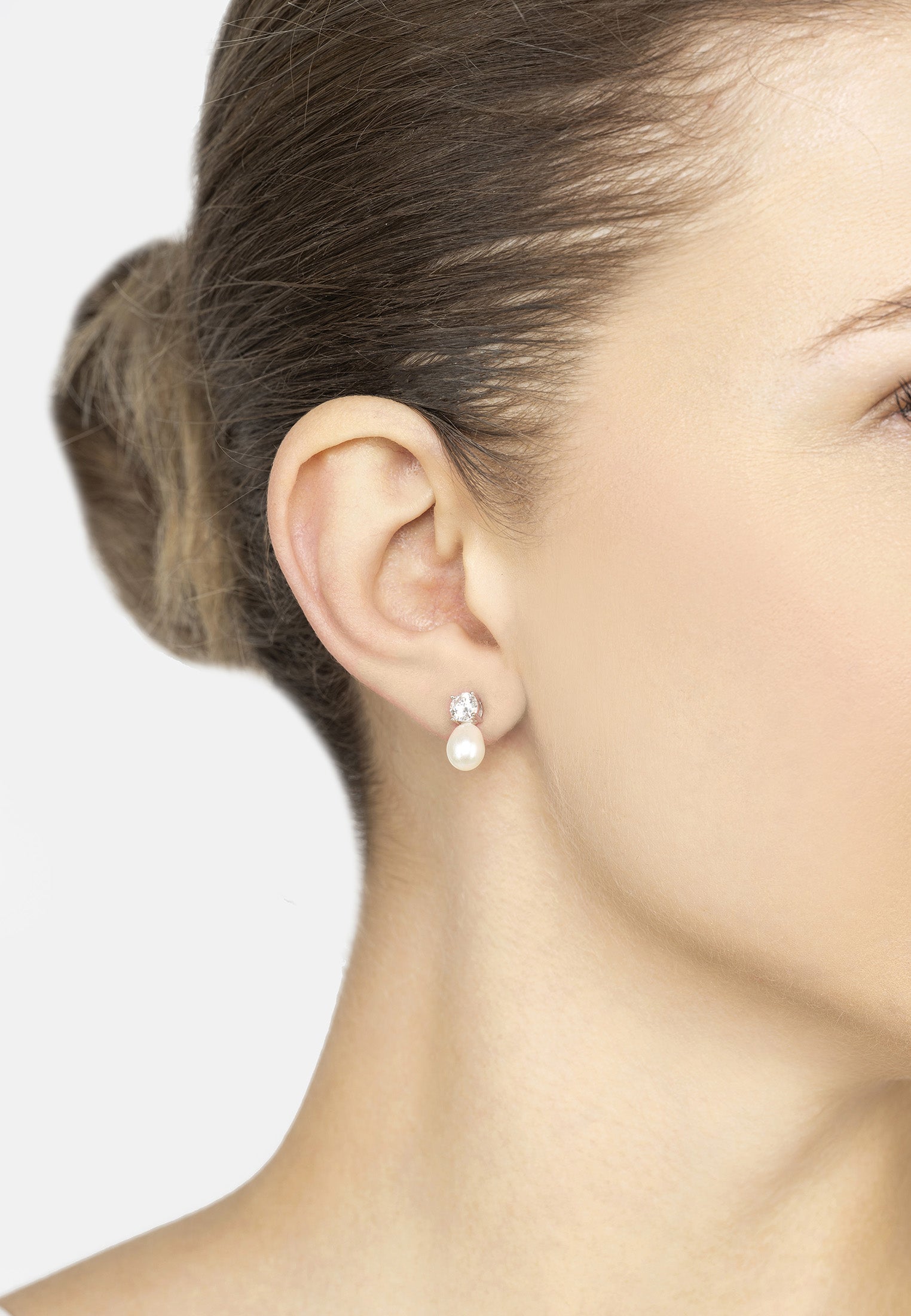 Close-up of a woman wearing pearl earrings with a plain background