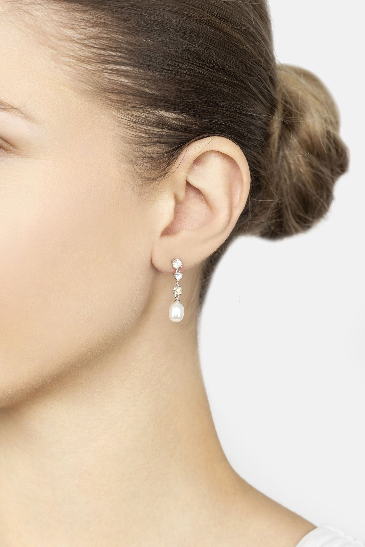Close-up of a person wearing a pearl drop earring with a white background
