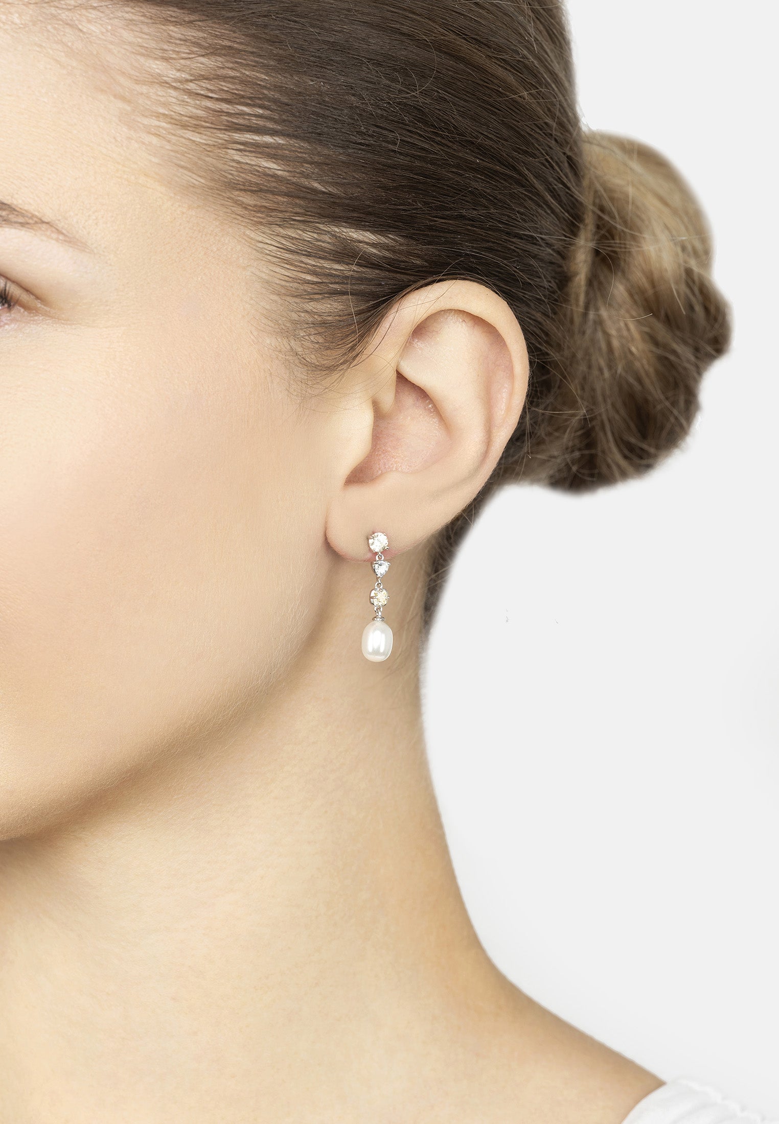 Close-up of a person wearing a pearl drop earring with a white background
