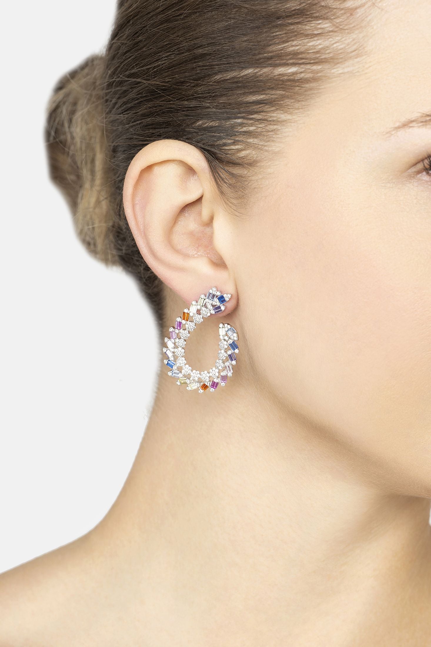 Close-up of a woman wearing colorful hoop earrings against a neutral background
