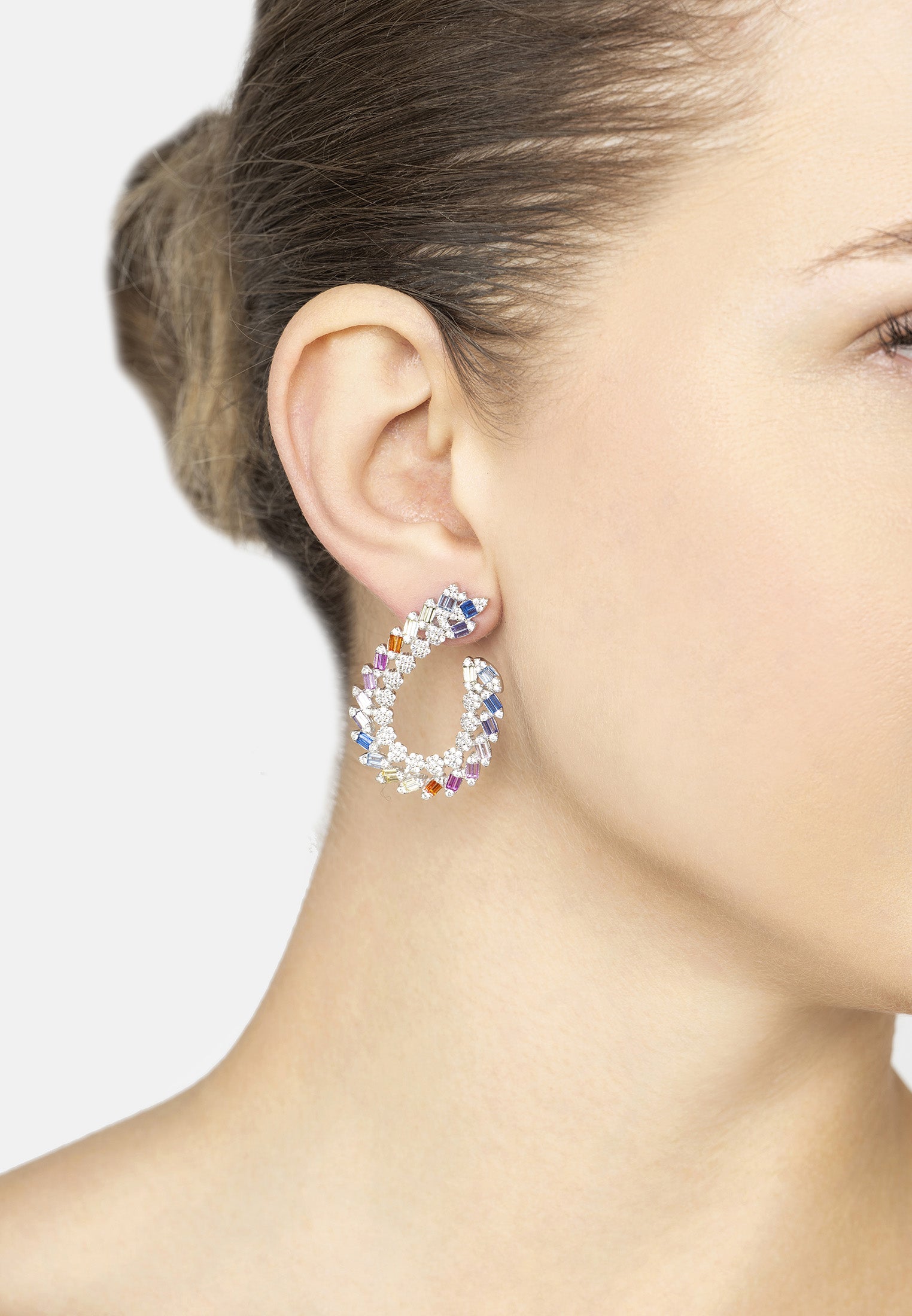 Close-up of a woman wearing colorful hoop earrings against a neutral background