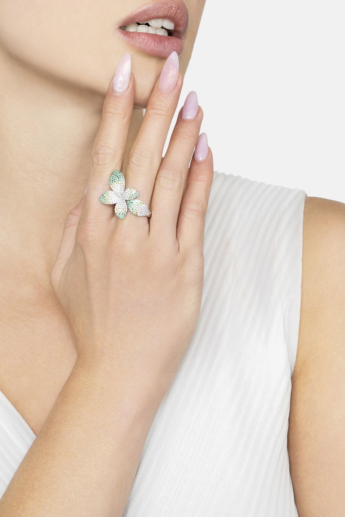 Leaf-shaped ring with gemstones on a hand against a neutral background