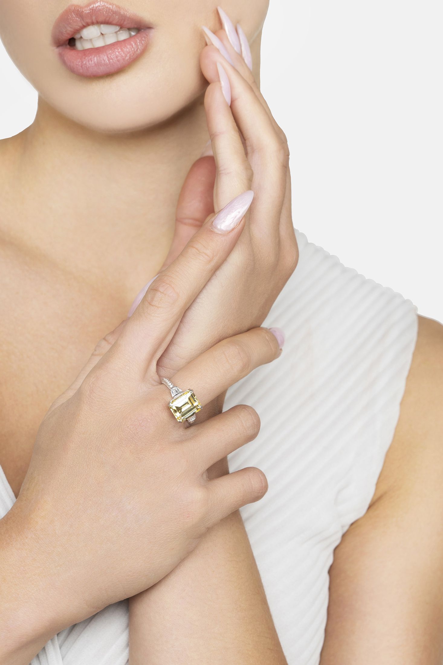Close-up of a hand wearing a gold ring with a yellow gemstone, against a neutral background.