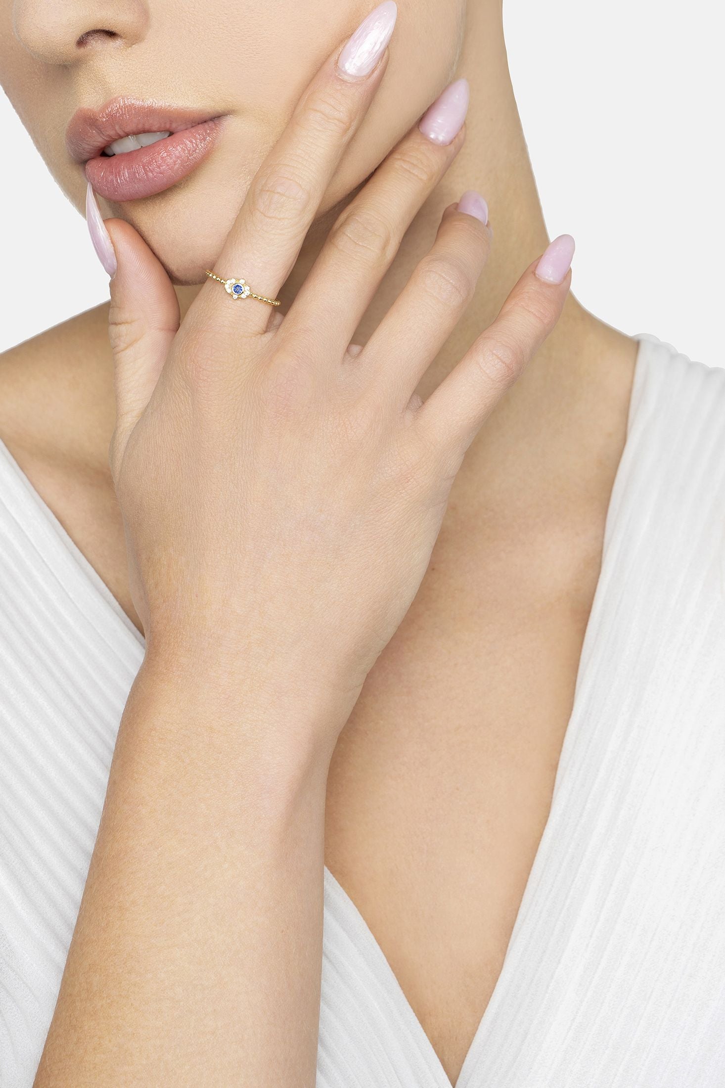 Close-up of a hand wearing a ring with a blue gemstone, against a neutral background.
