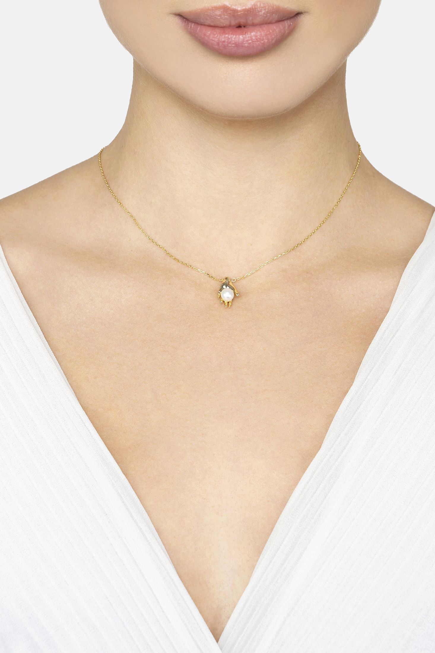 Gold necklace with a small pendant on a model wearing a white top.