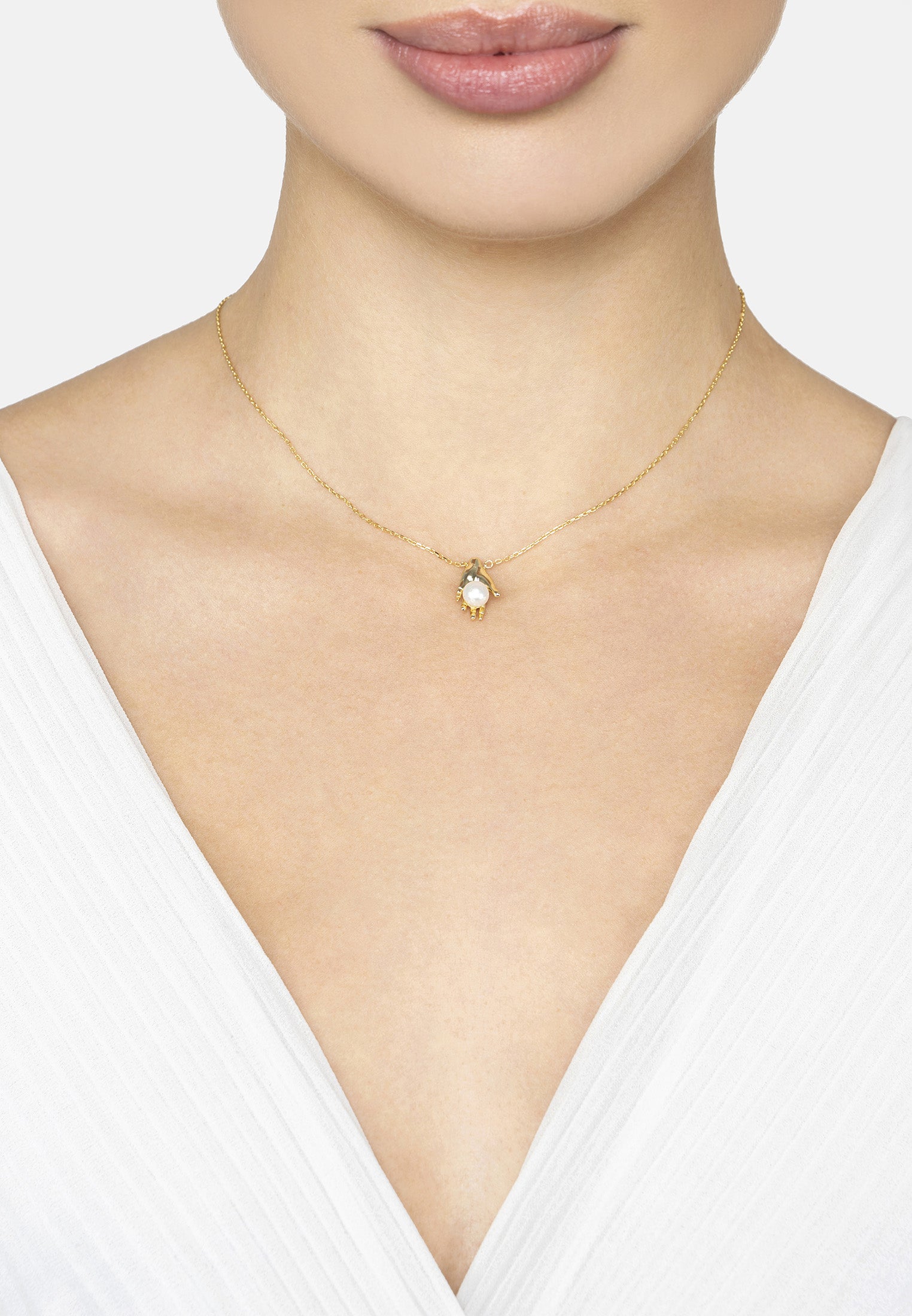 Gold necklace with a small pendant on a model wearing a white top.