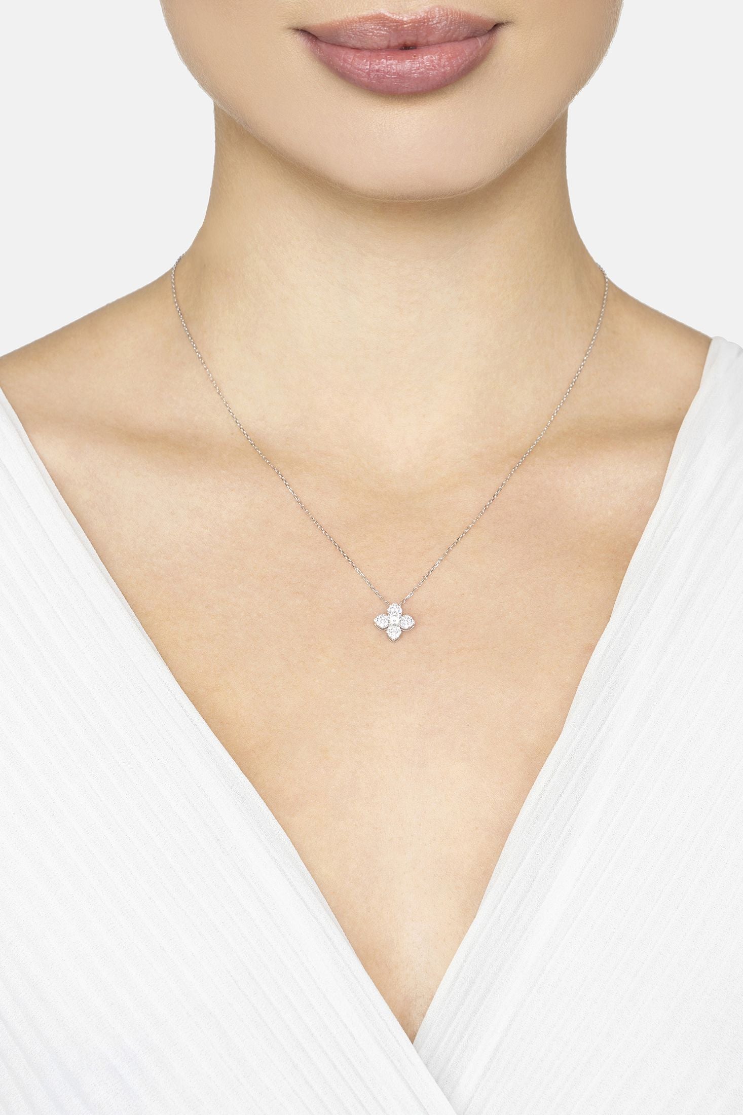 Necklace with a delicate clover pendant worn by a person in a white top on a light background