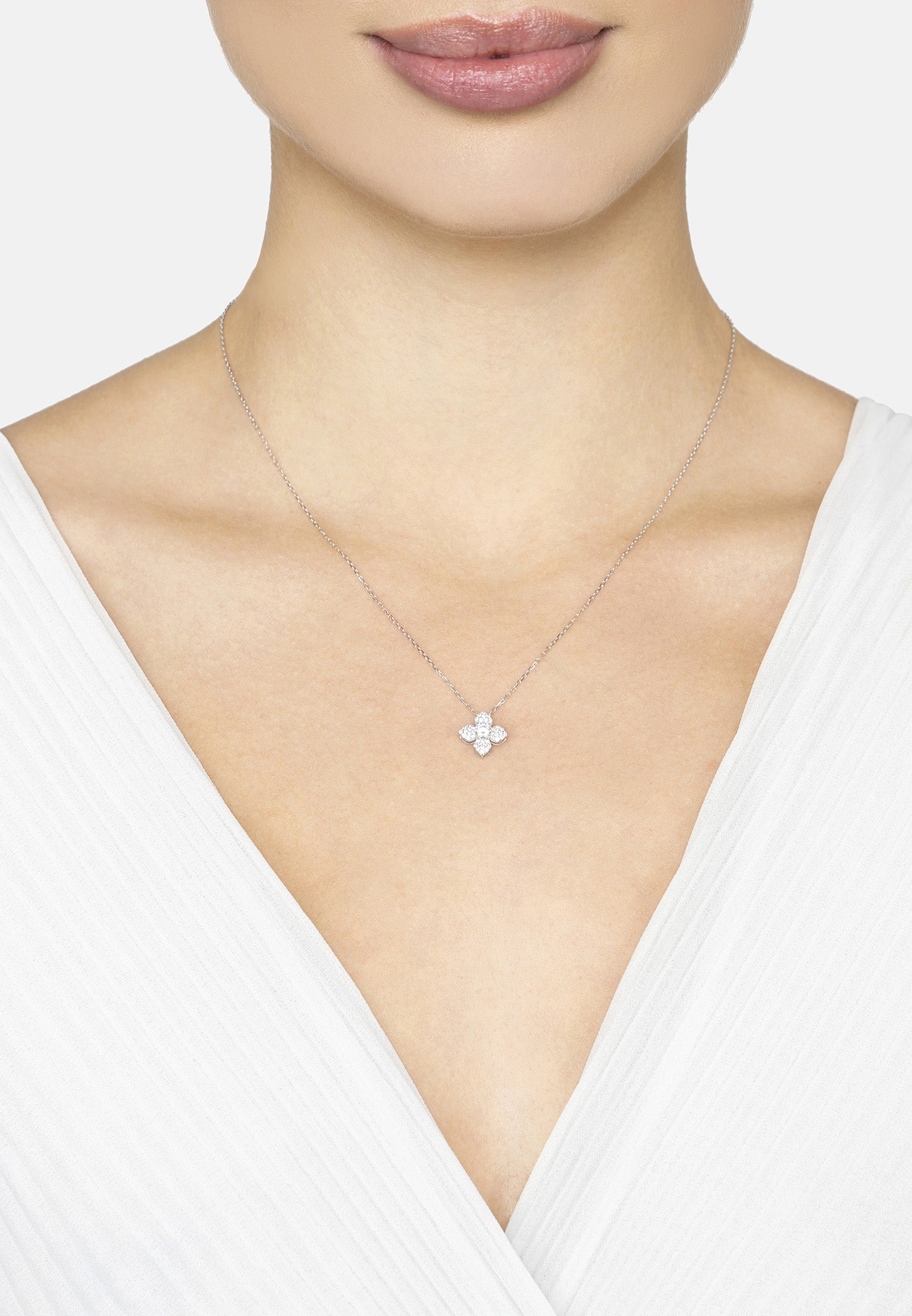 Necklace with a delicate clover pendant worn by a person in a white top on a light background