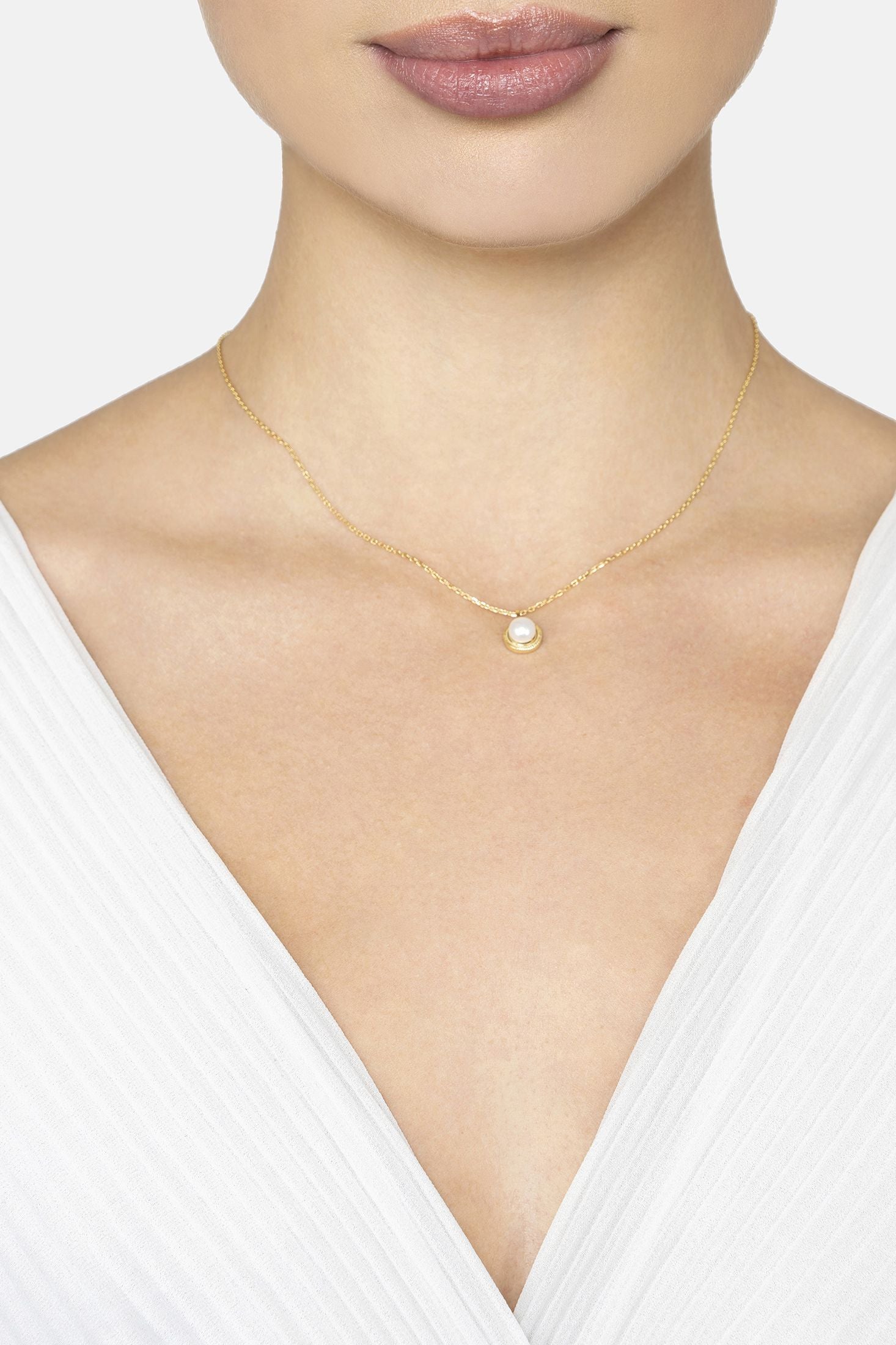 Gold necklace with a pearl pendant worn by a model against a white background