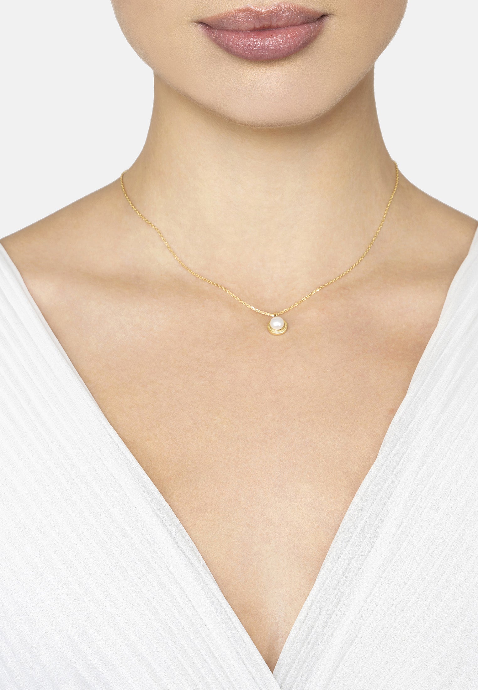 Gold necklace with a pearl pendant worn by a model against a white background