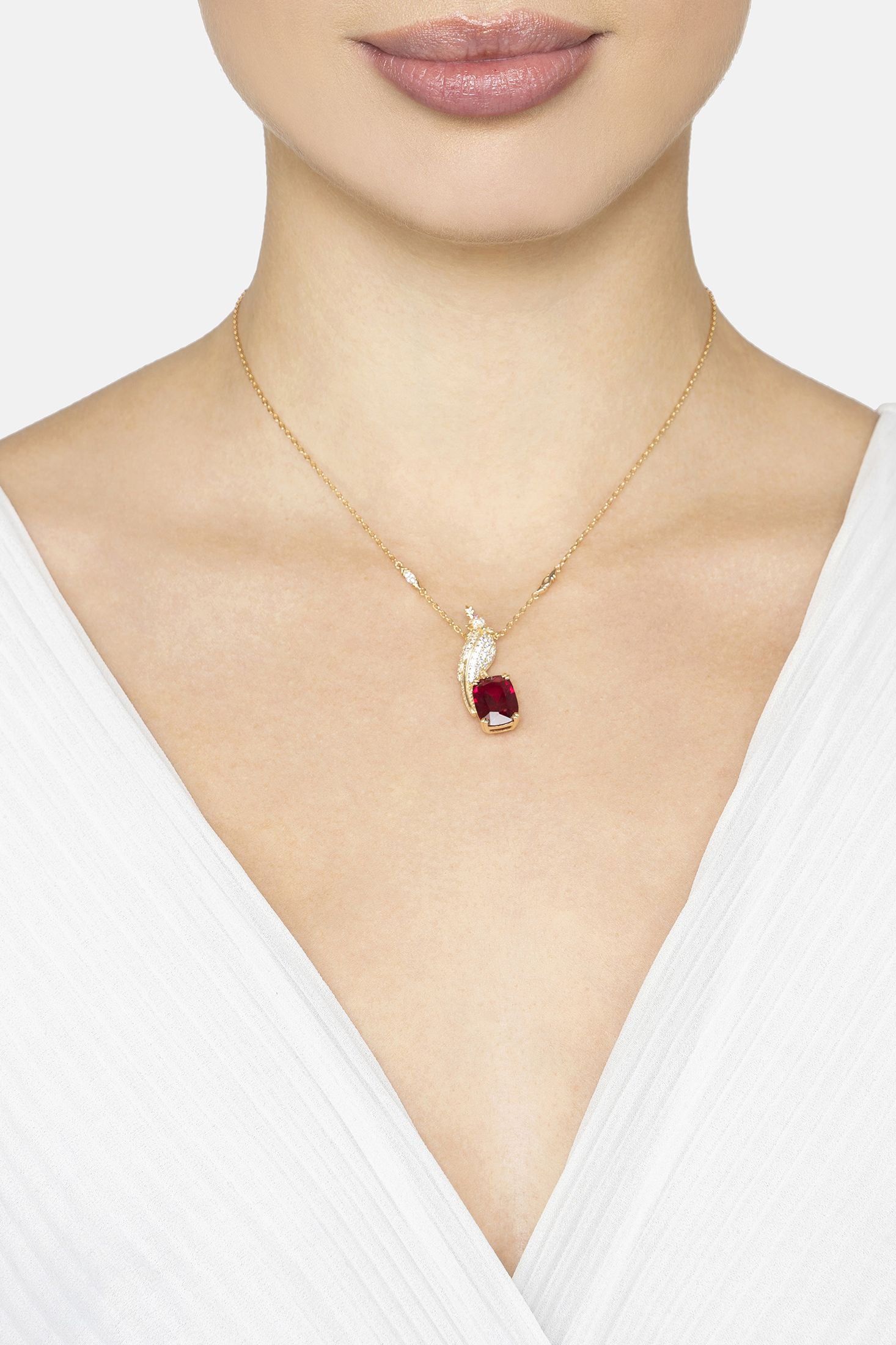 Gold necklace with a red bird shaped pendant worn by a person in a white top.
