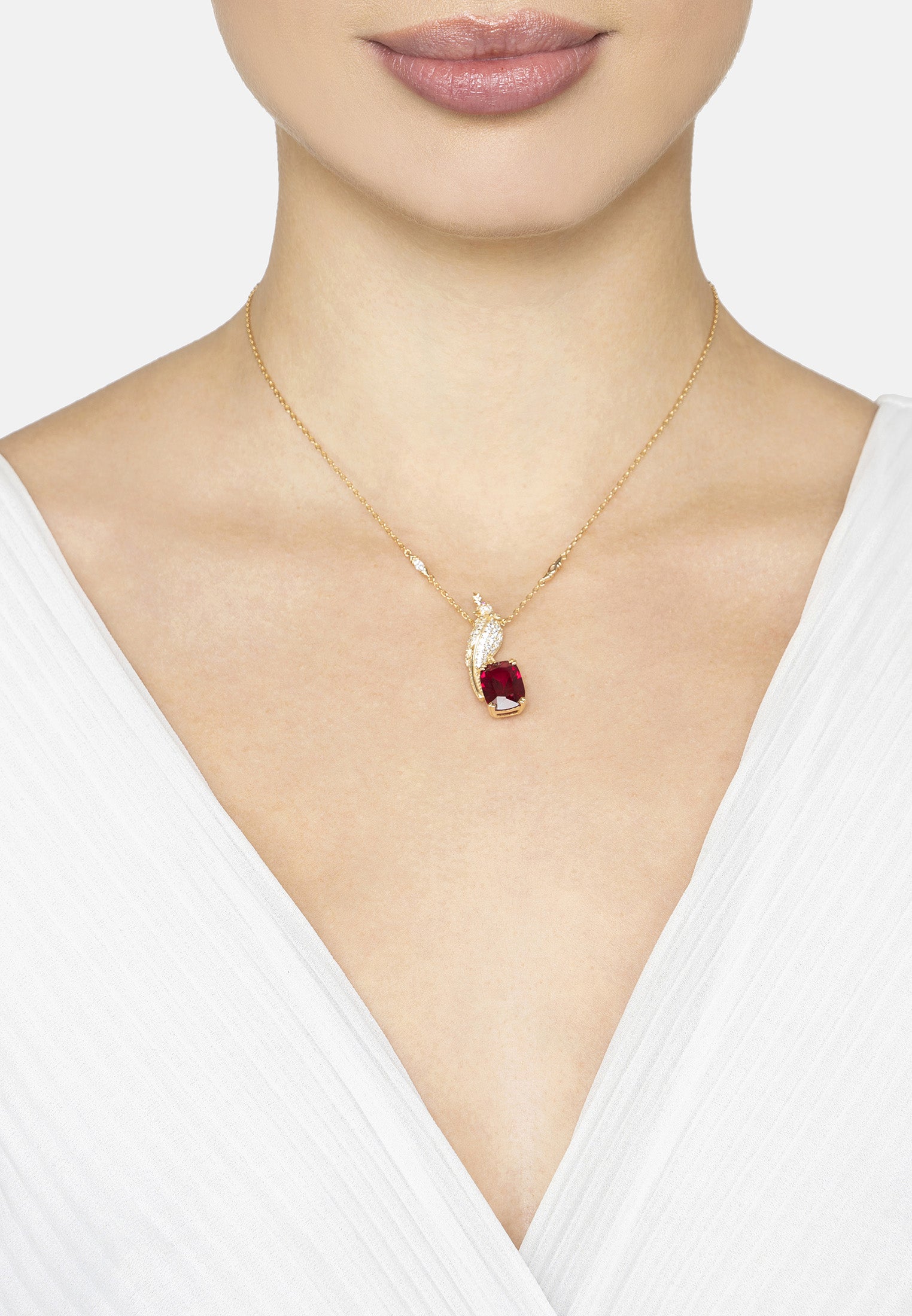 Gold necklace with a red bird shaped pendant worn by a person in a white top.