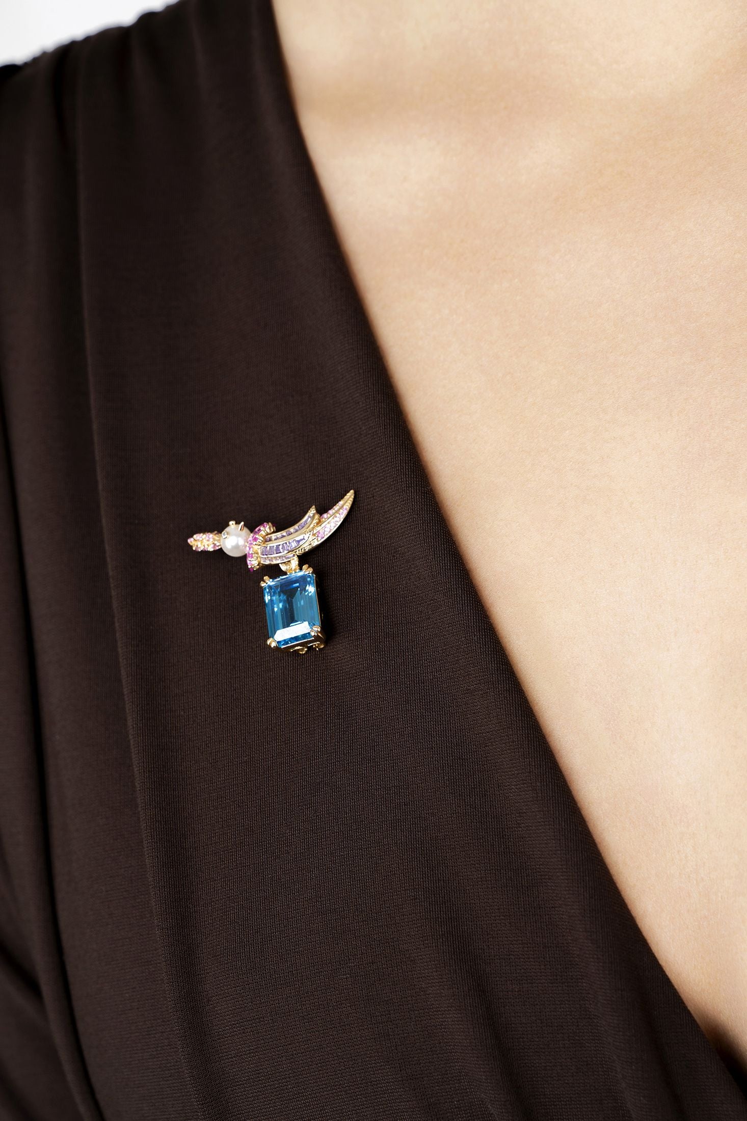 Brooch with blue gemstone and gold accents on a black garment