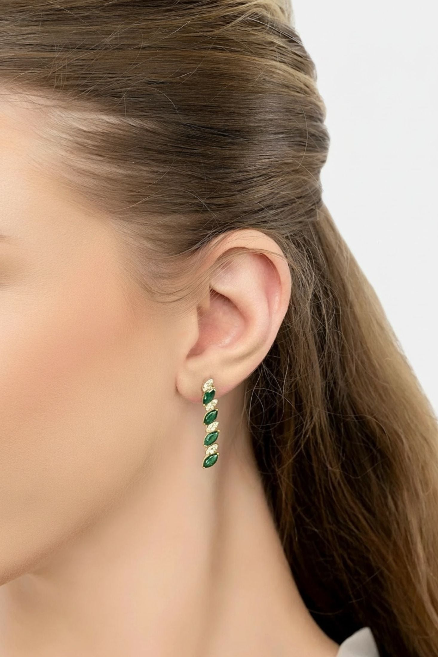 Gold and green drop earrings worn by a model.