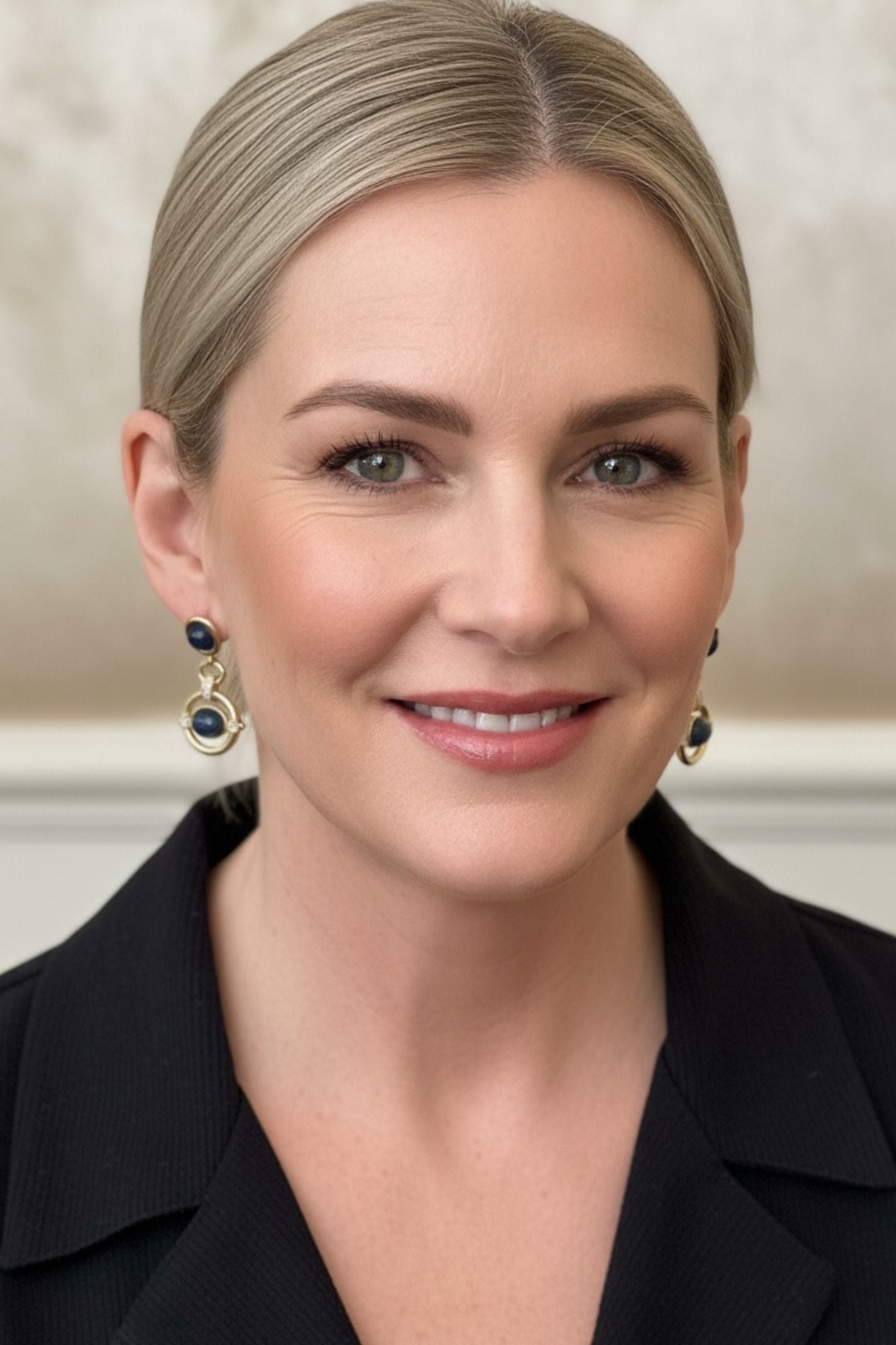 Woman wearing a black blazer and gold drop earrings with blue gemstones