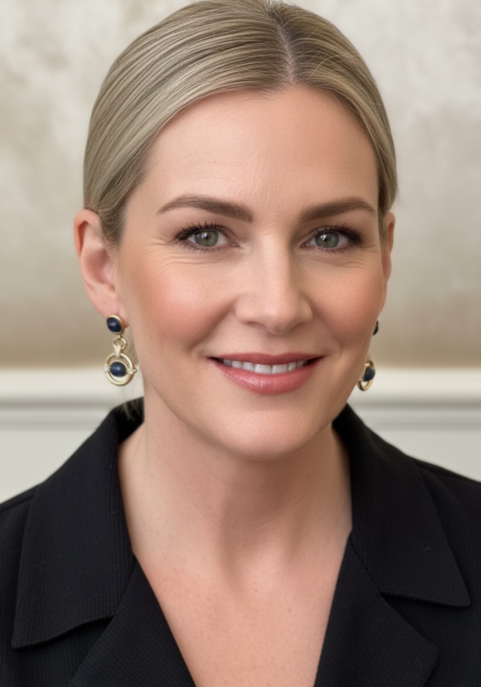 Woman wearing a black blazer and gold drop earrings with blue gemstones