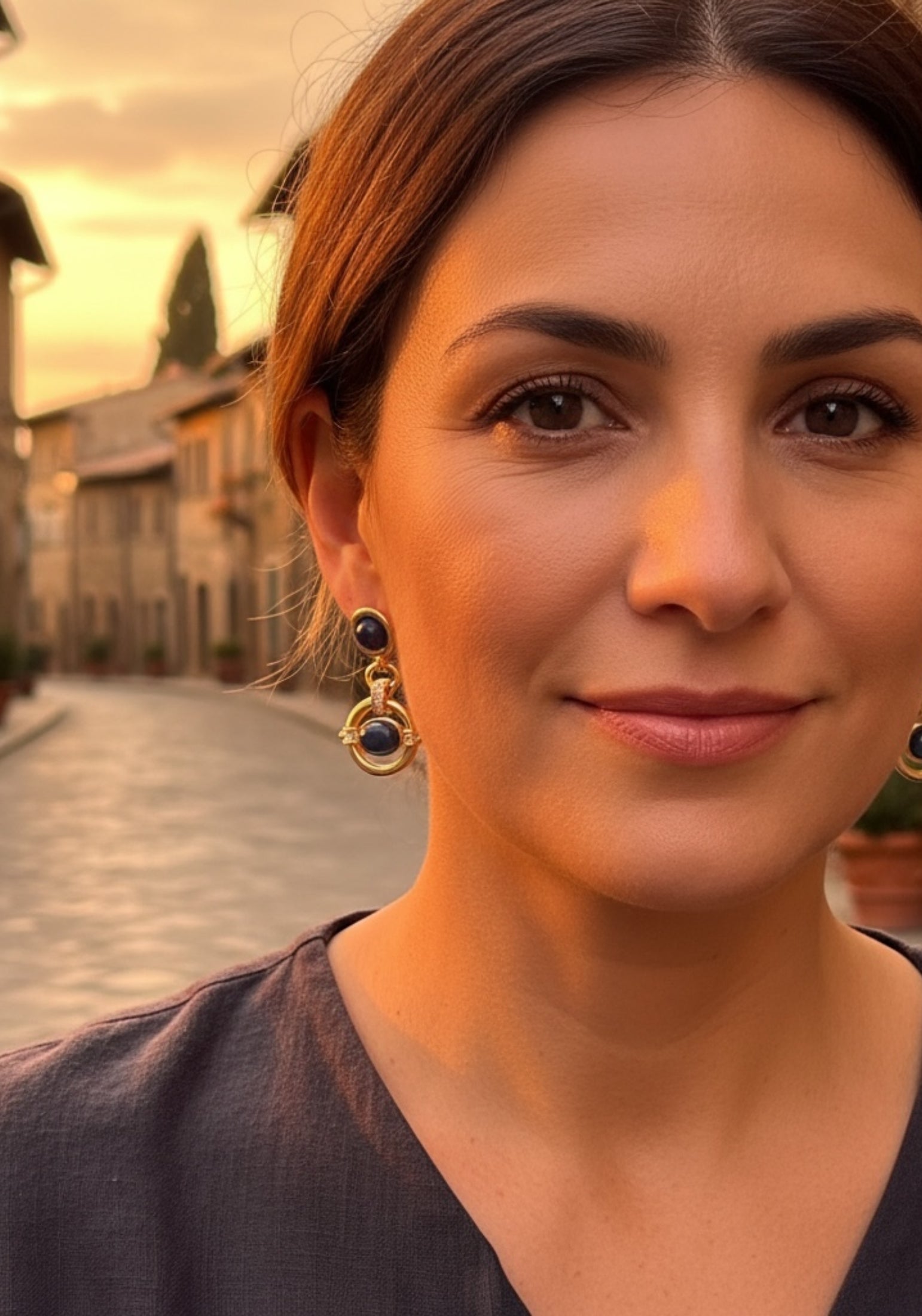 Woman with earrings standing in a street wearing gold earrings with blue gemstones