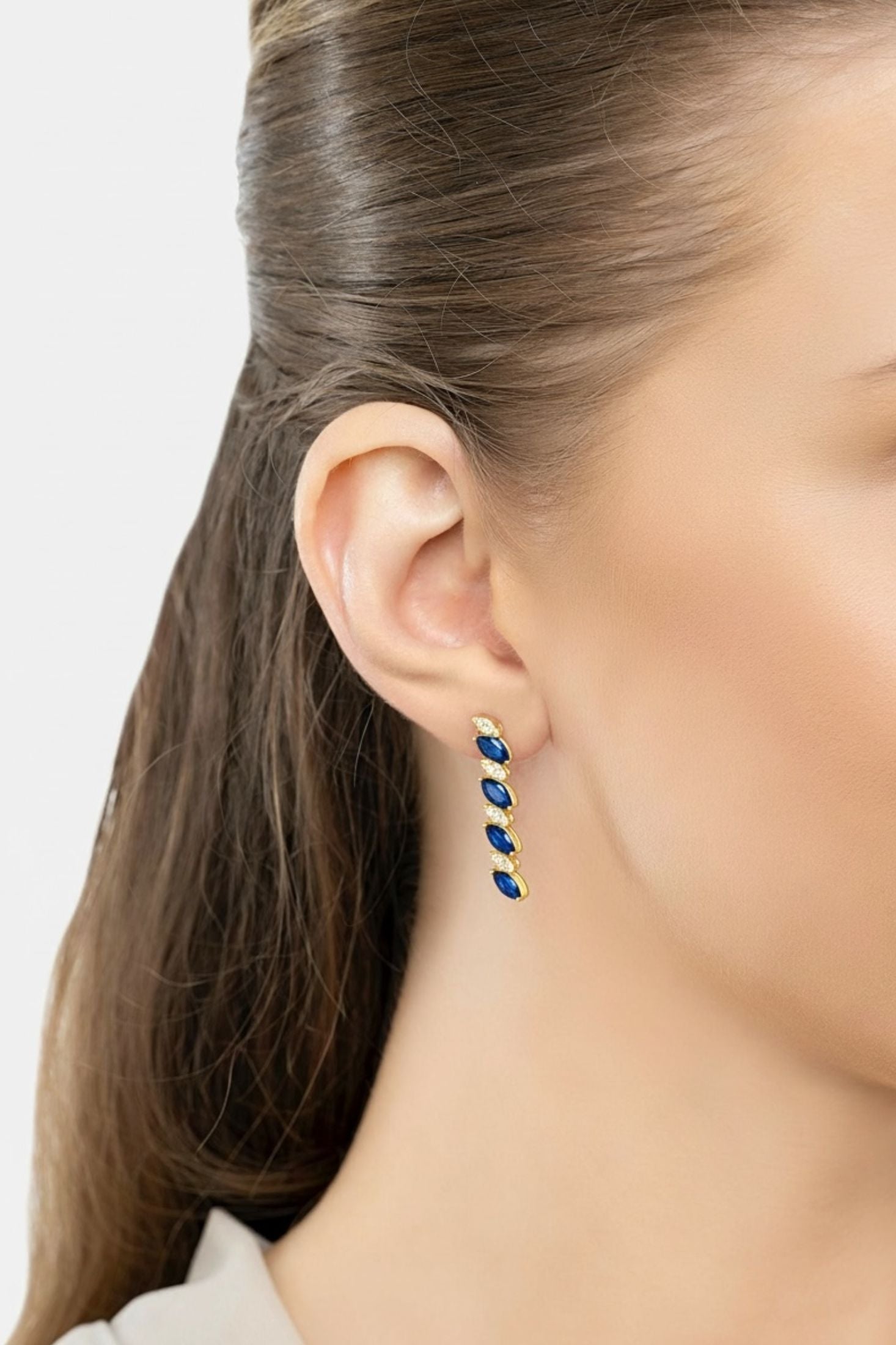 Gold and blue drop earrings worn by a model.