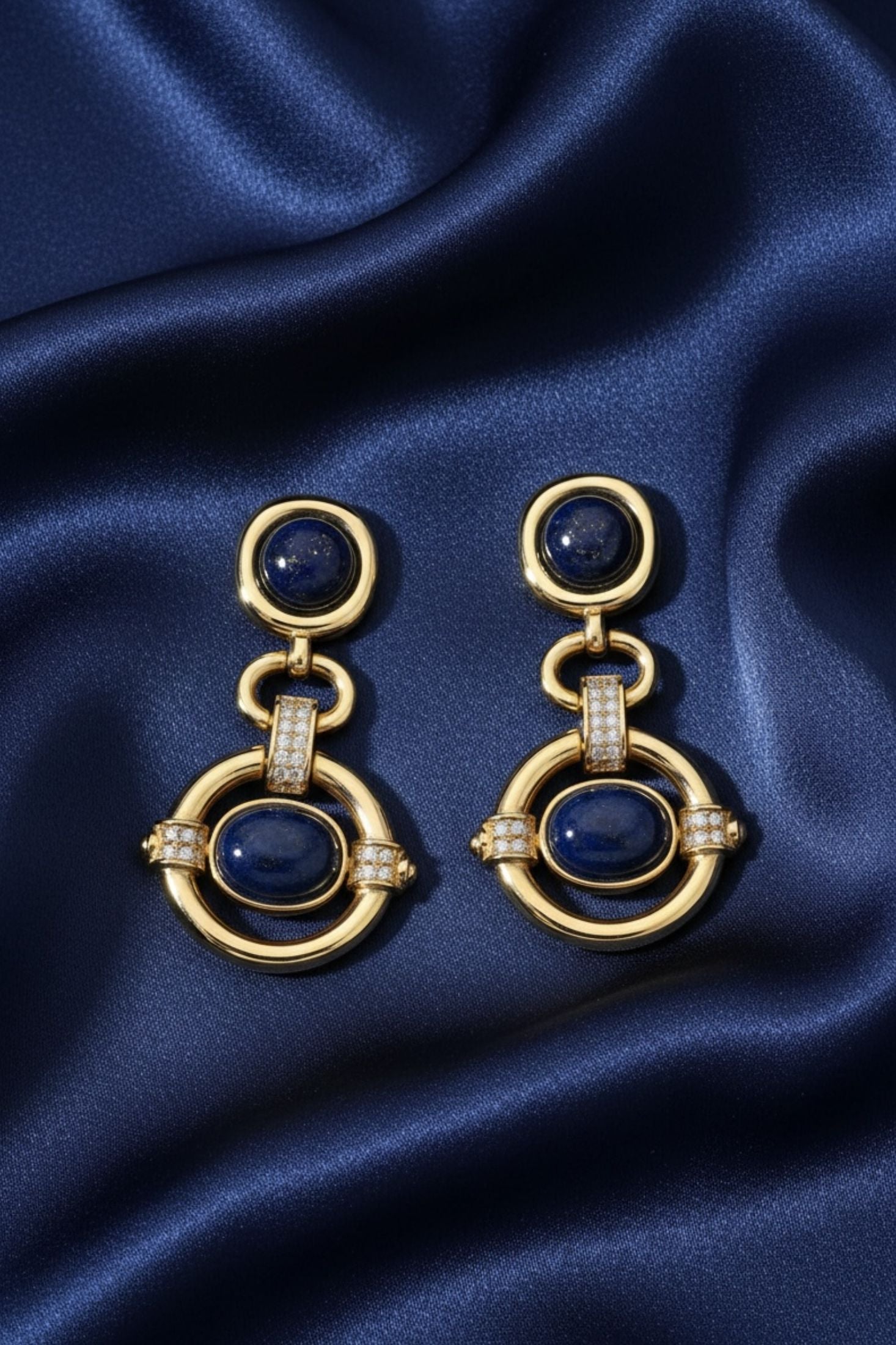 Gold earrings with blue stones on a blue satin background