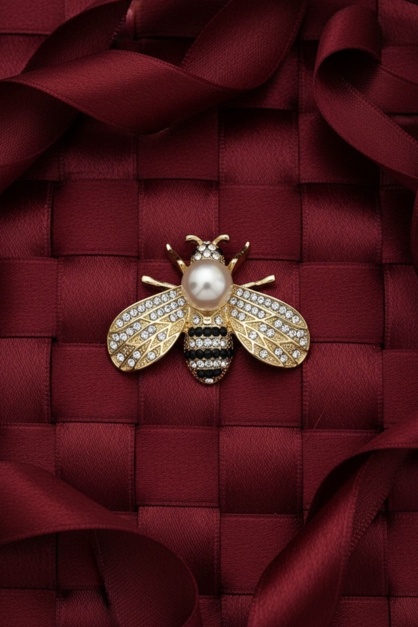 Gold bee-shaped brooch with a pearl on a red textured fabric background