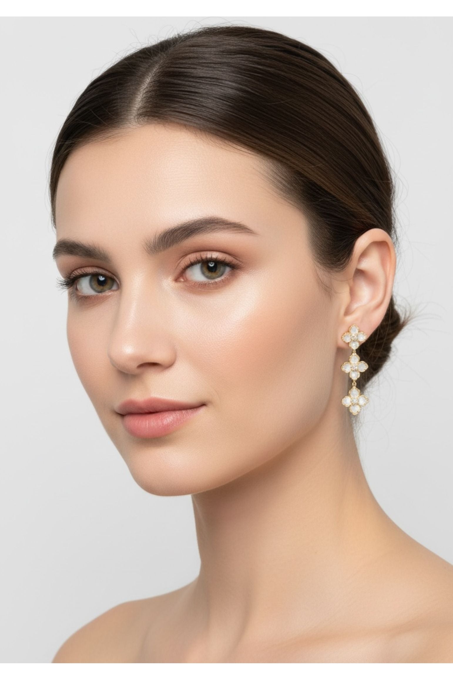 Woman wearing white clover earrings on a plain background
