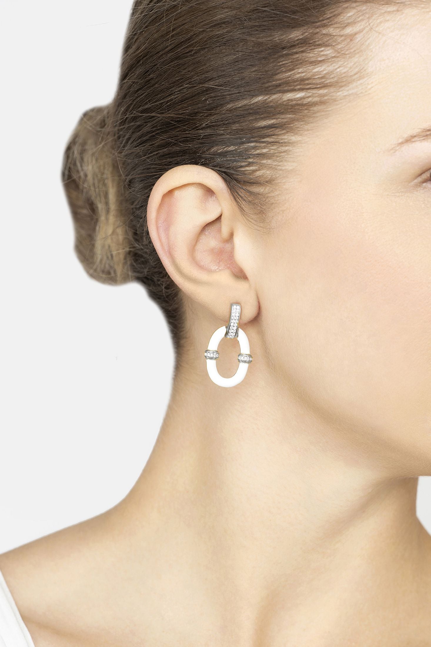 Silver hoop earring worn by a person on a plain background