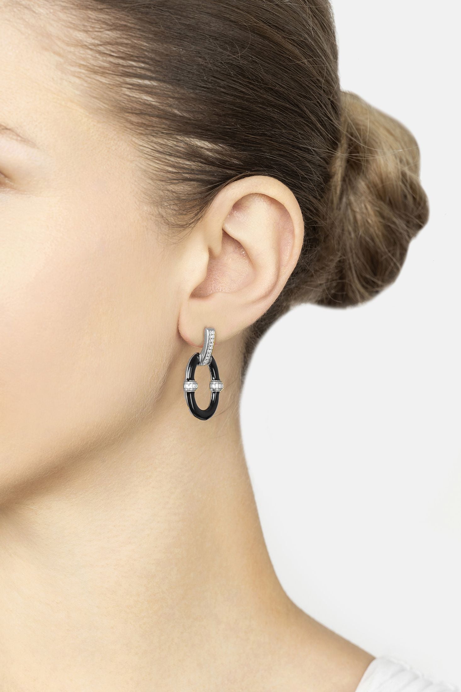 Close-up of a person wearing a silver hoop earring with a black center on a white background