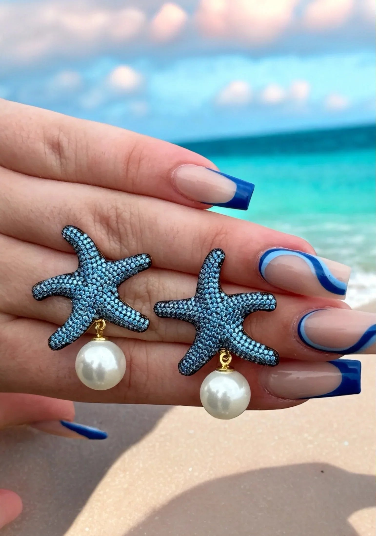 The earrings held up by a hand model.