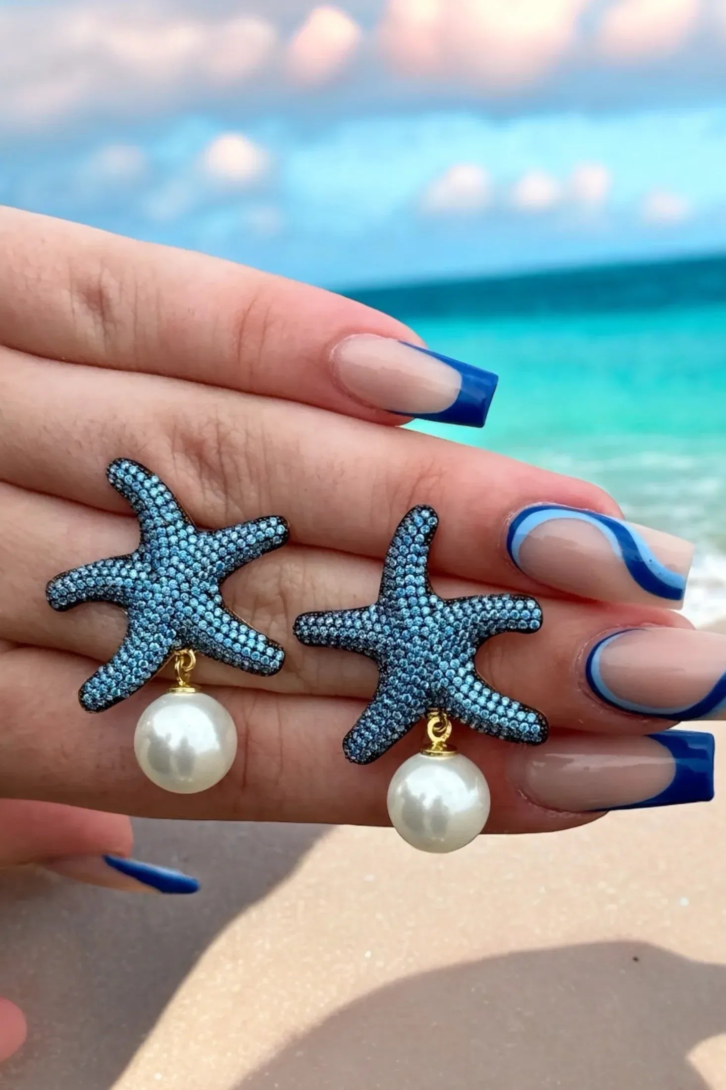 The earrings held up by a hand model.