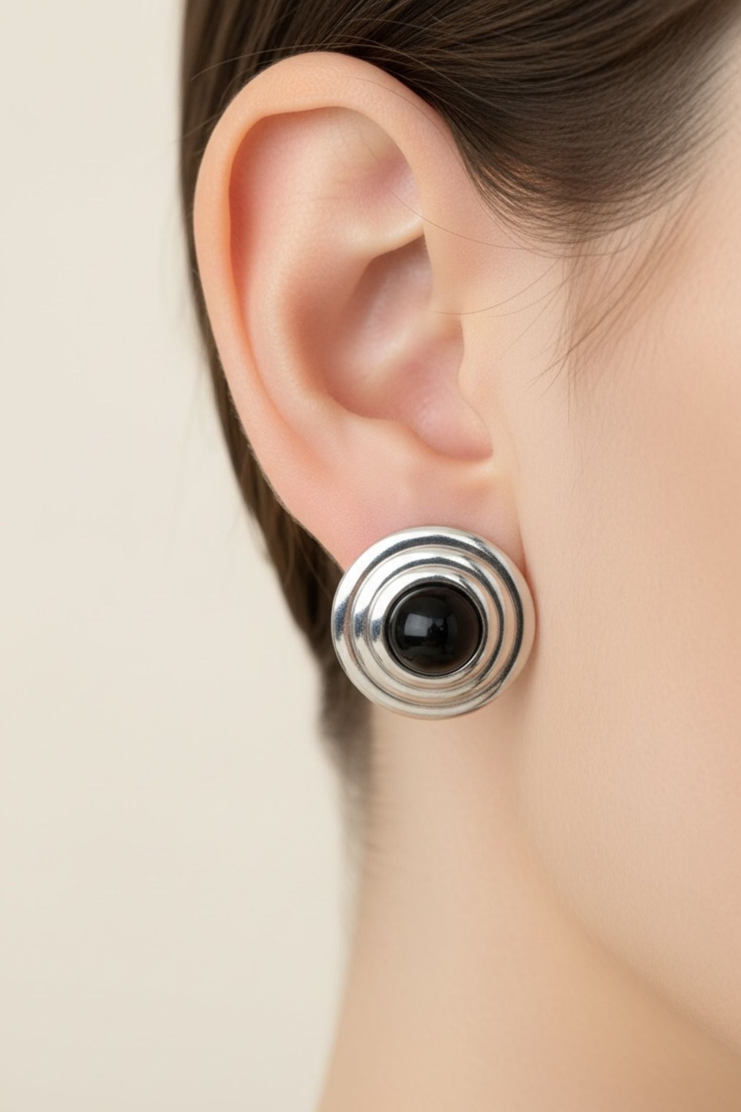 Close-up of an ear wearing a silver and black earring against a neutral background