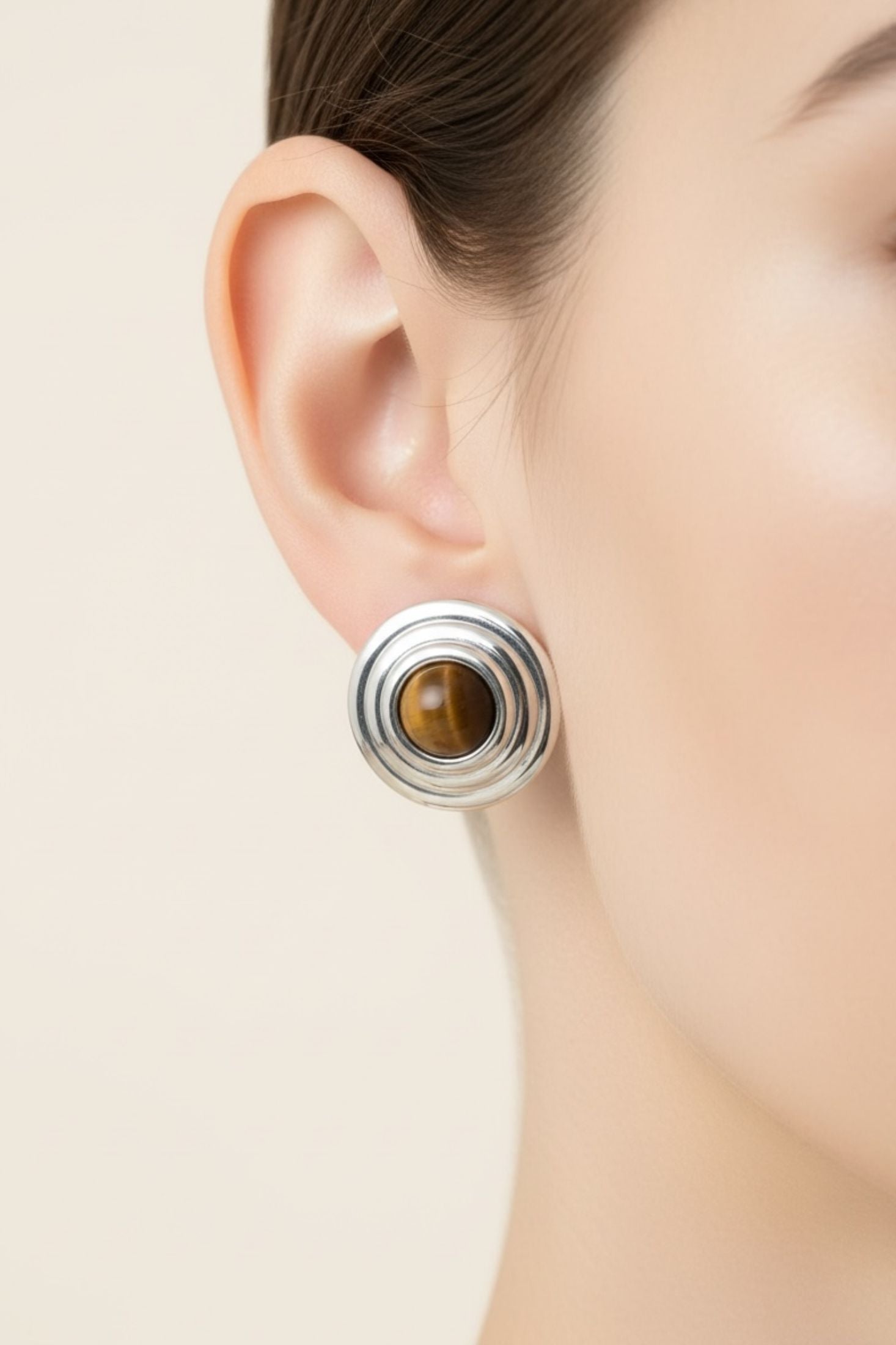 Close-up of an ear wearing a silver earring with a tigers eye gemstone on a white background