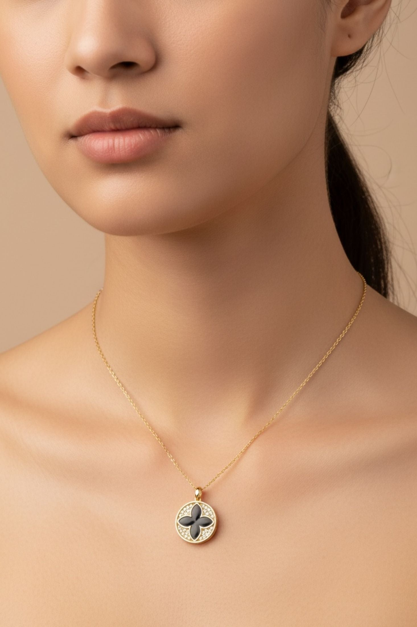 Close-up of a person wearing a gold necklace with a clover pendant on a beige background