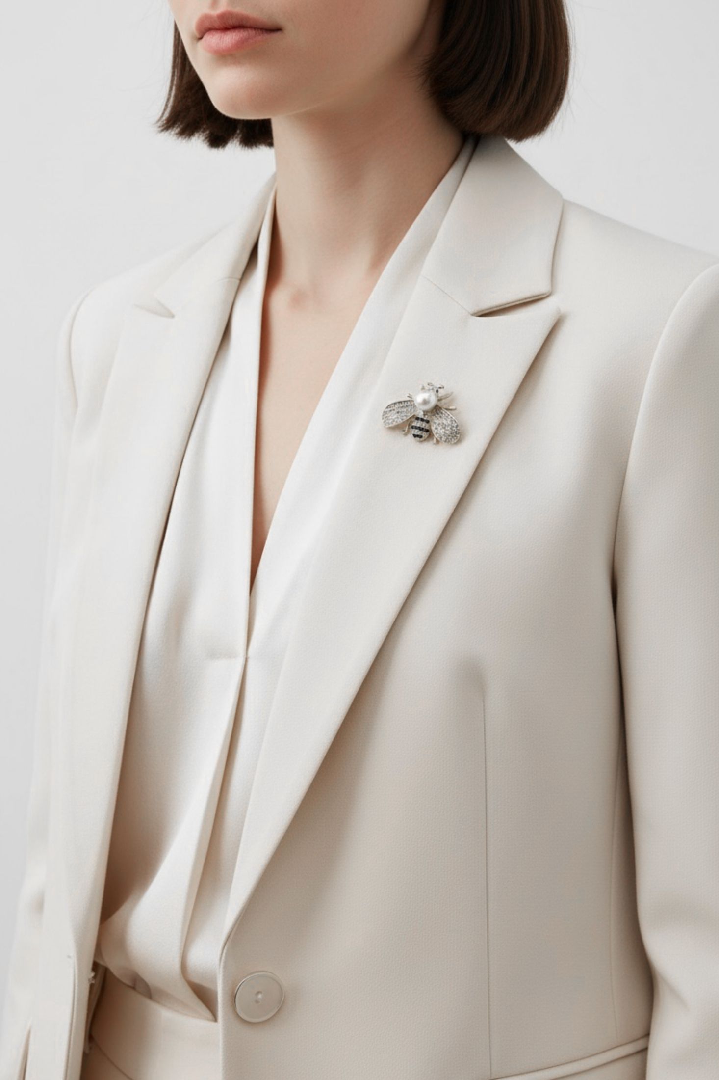 Person wearing a beige blazer with a decorative bee brooch on a light background