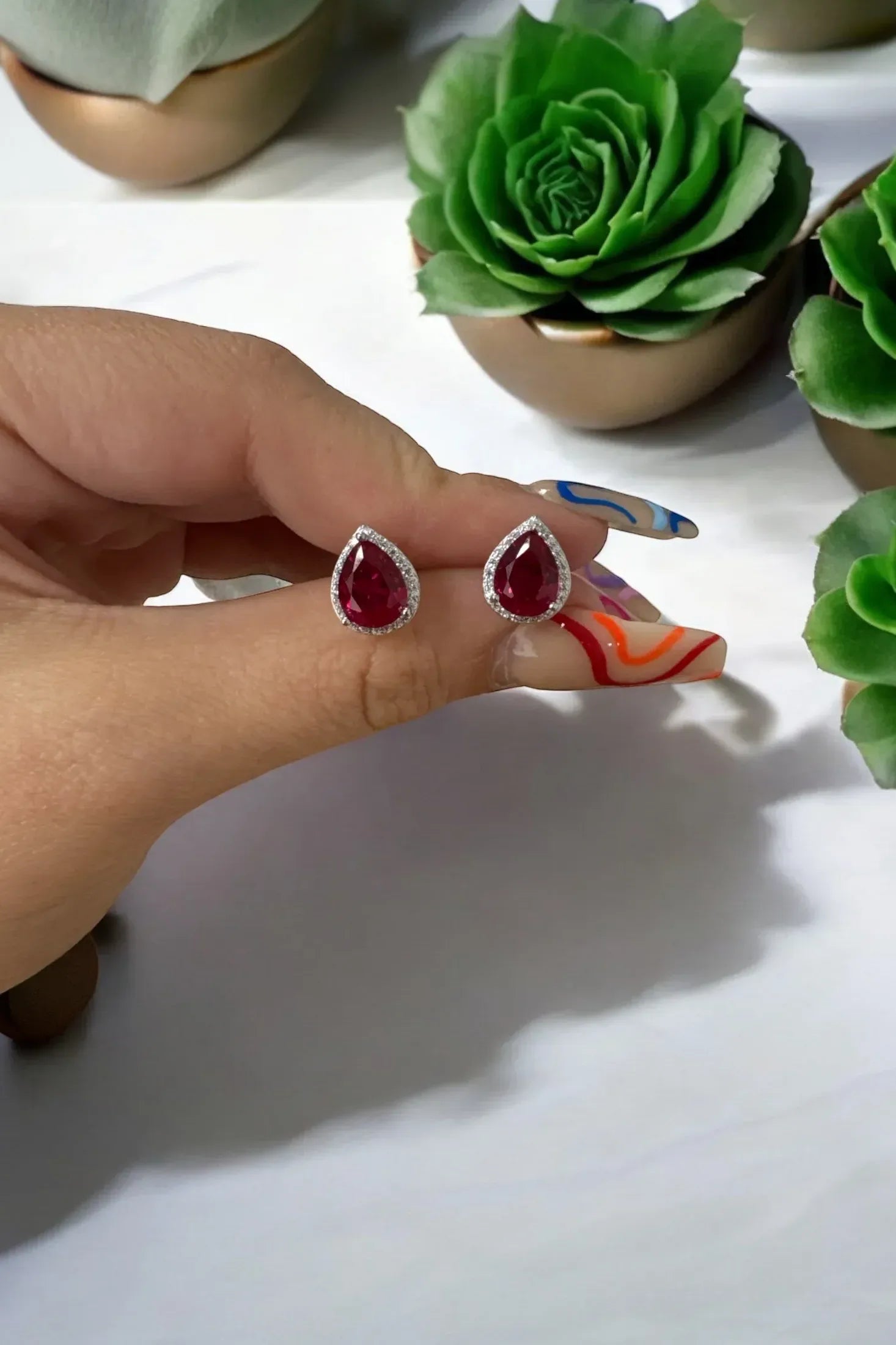 The earrings held up by a hand model.