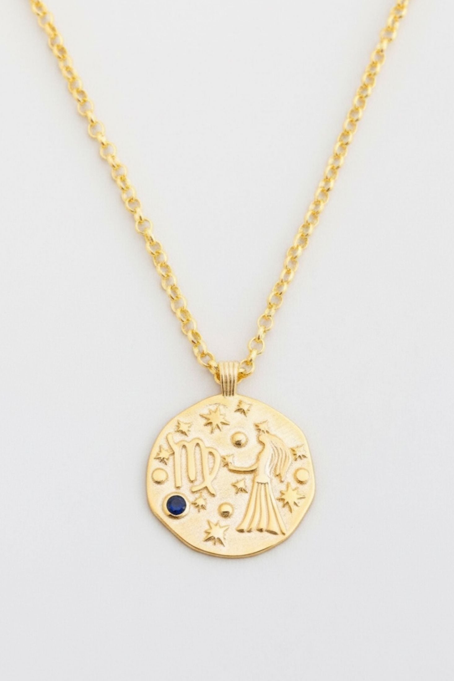 Gold necklace with a circular pendant featuring astrological design on a light gray background