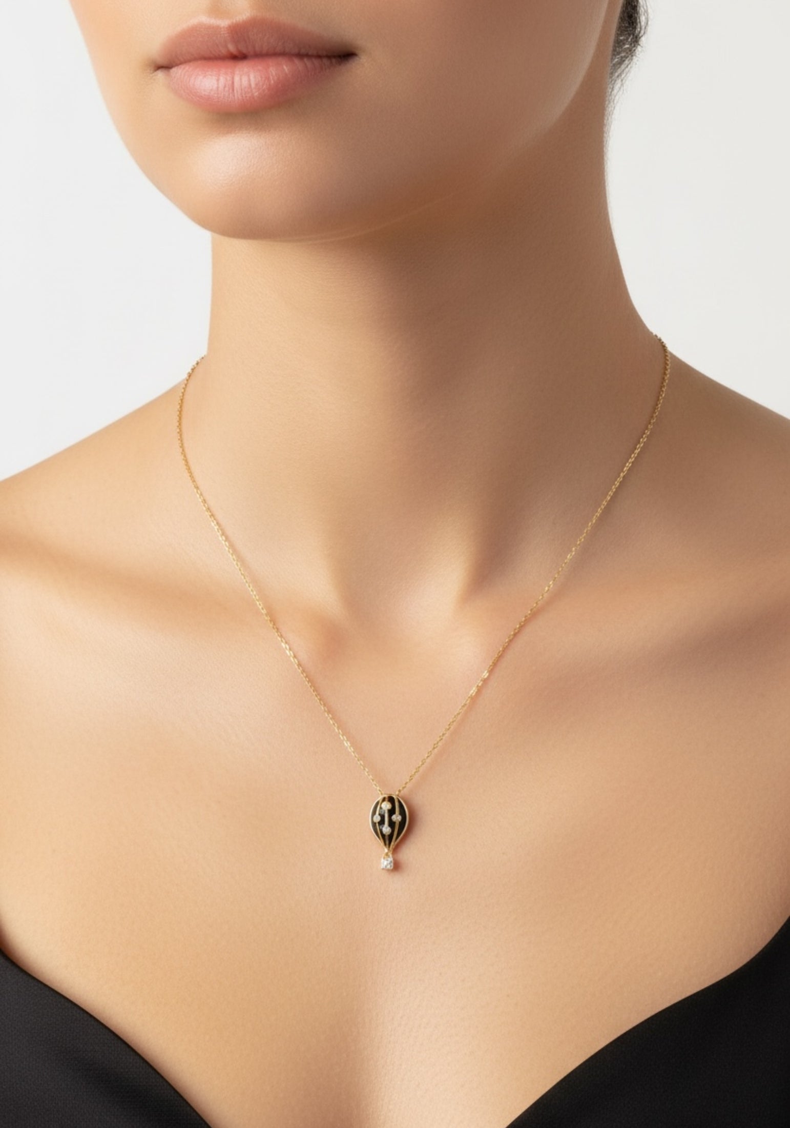 Gold necklace with a black hot air balloon pendant on a model against a neutral background